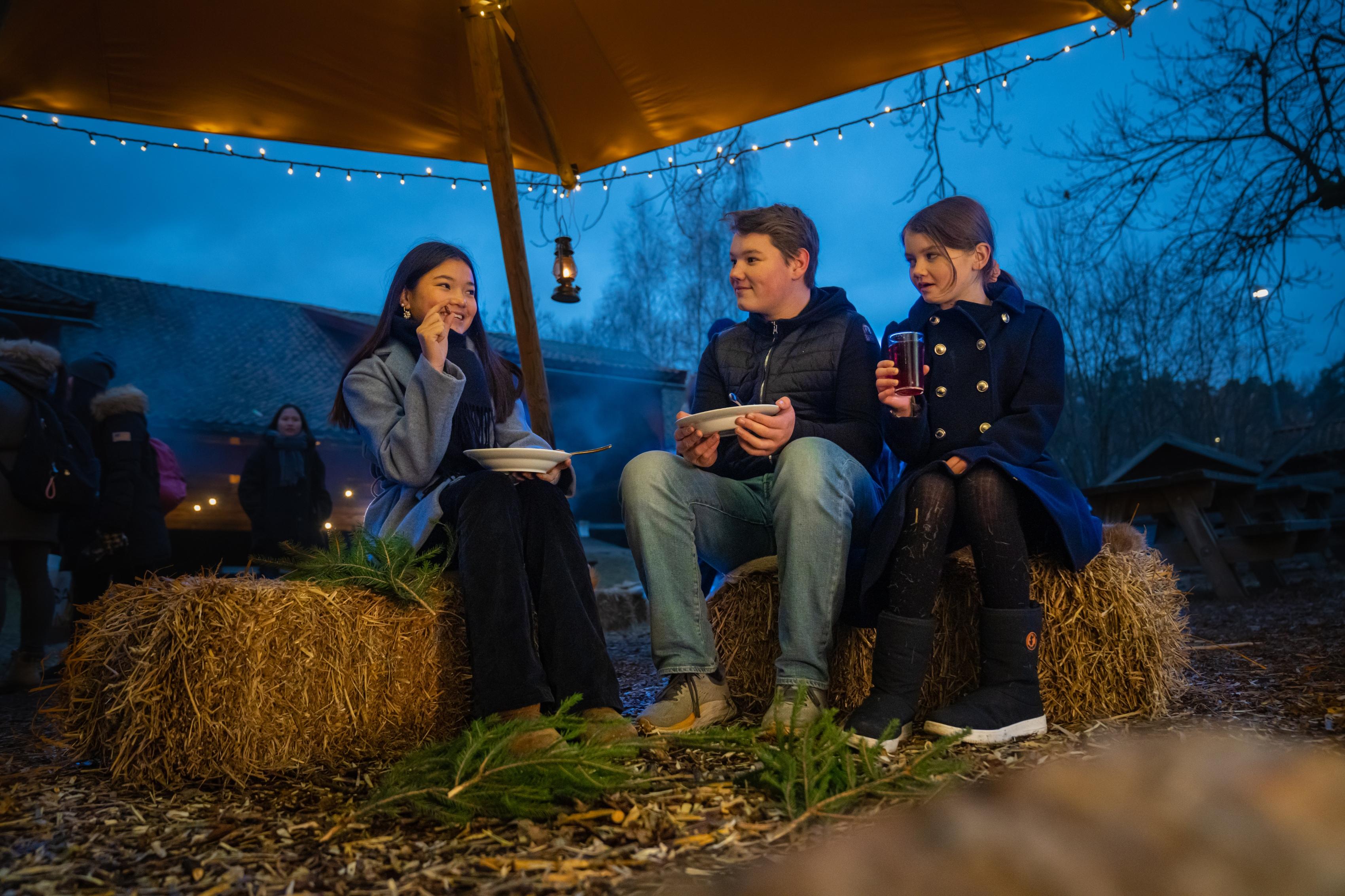 Three kids are eating porridge at the Christmas market in Norsk Folkemuseum in Bygdøy, Eastern Norway