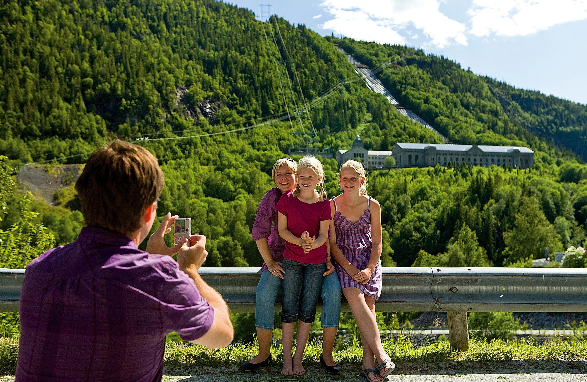 En person fotograferer tre barn foran Norsk industriarbeidermuseum i Vemork i Telemark