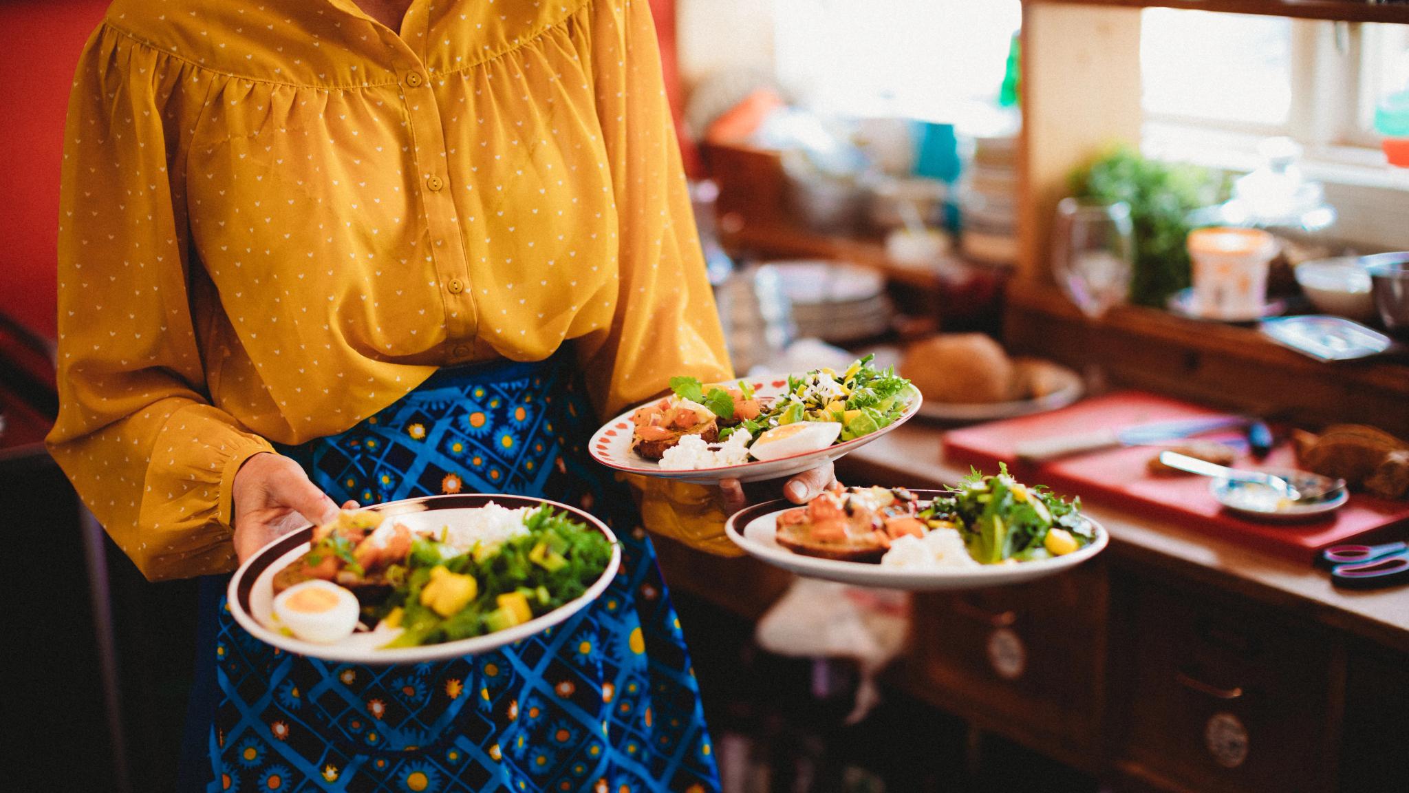 A woman carrying three plates of food at Sødahlhuset in Åndalsnes in Northwest, Fjord Norway.
