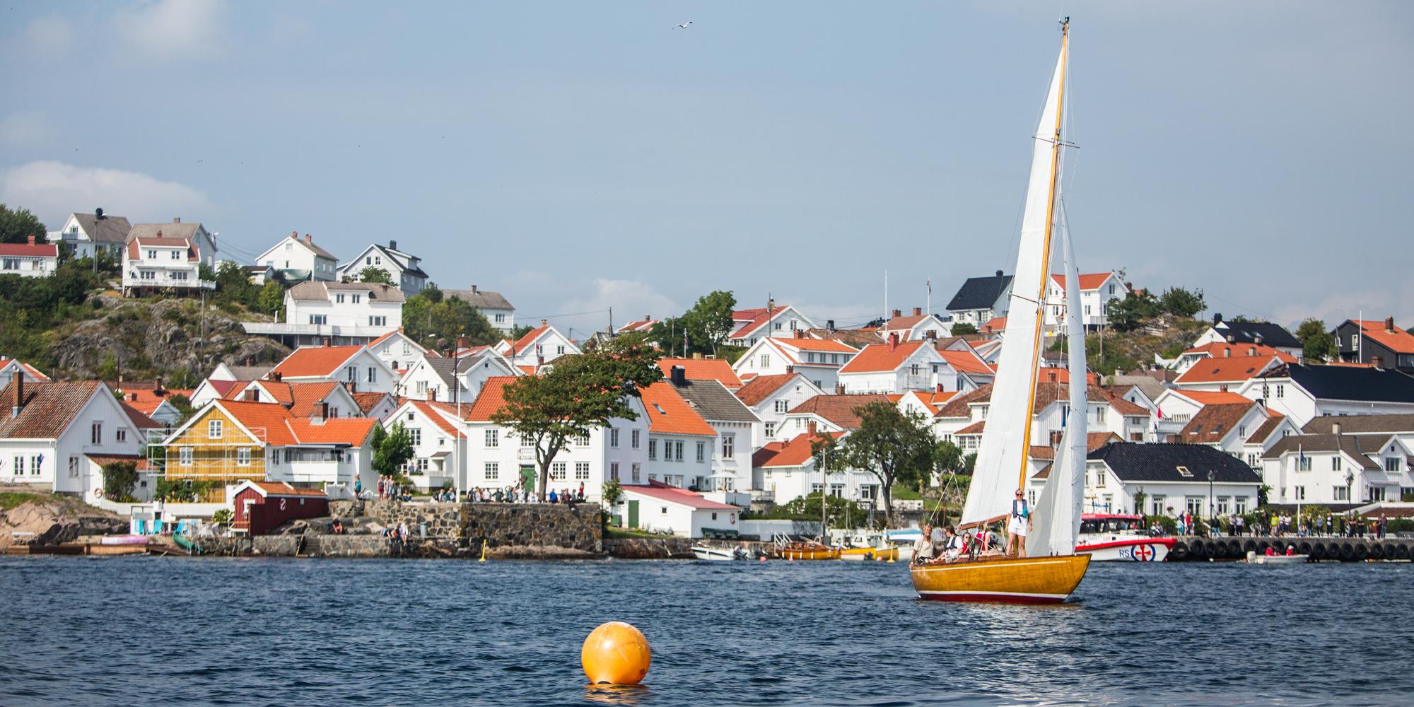 Ein hölzernes Segelboot vor weiß bemalten Holzhäusern in Risør, Südnorwegen