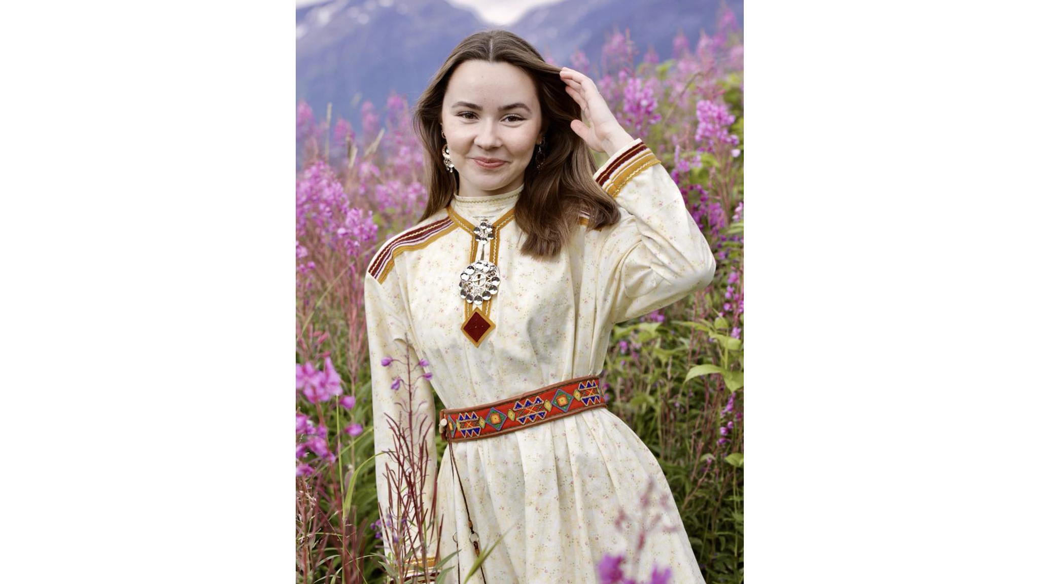 A young woman in a Sami summer kofte, surround by pink flowers