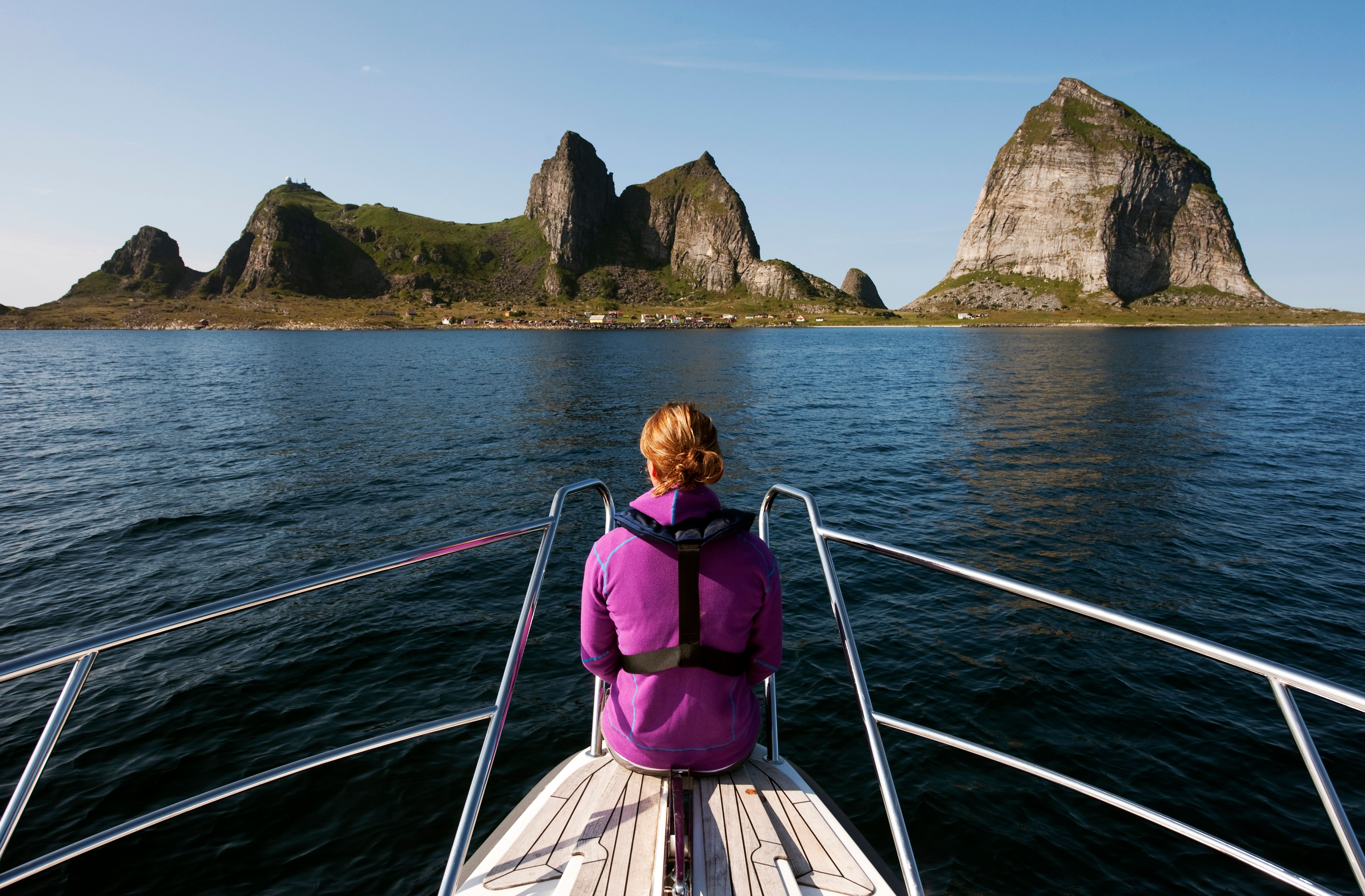 A woman sitting at the tip of a boat, looking out towards the mountains of Træna in Helgeland, Northern Norway.