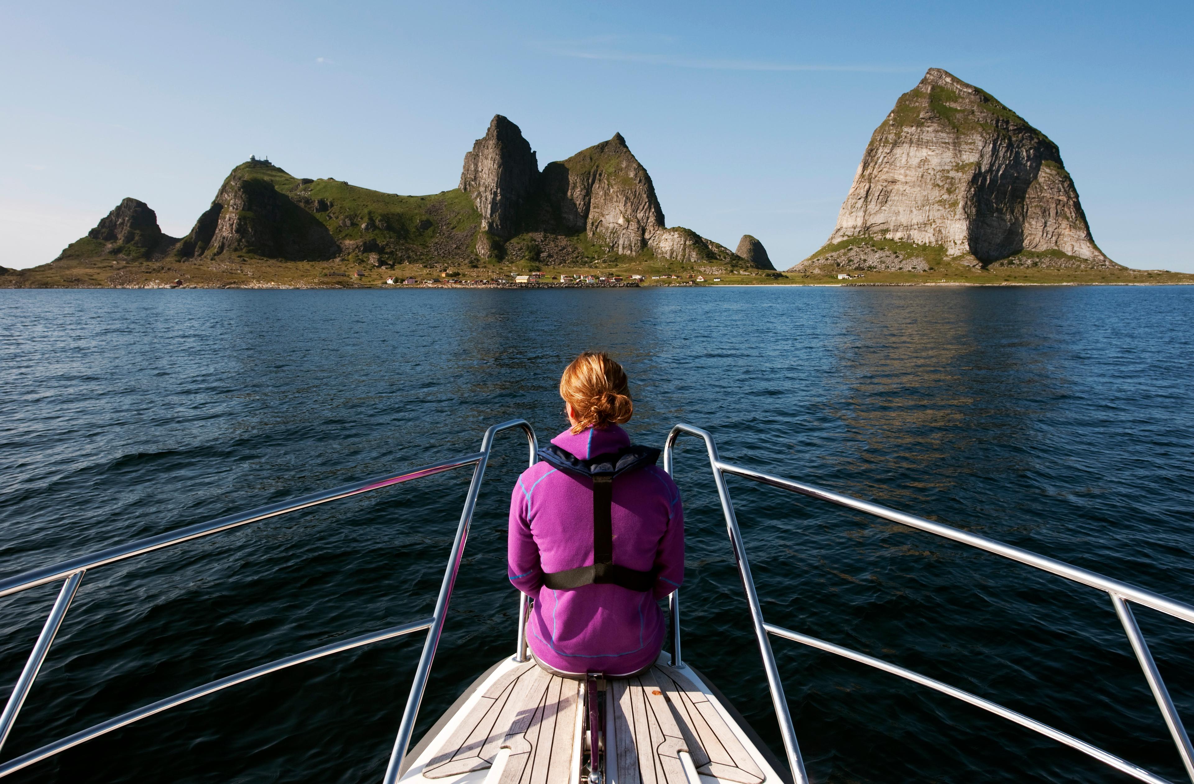 A woman sitting at the tip of a boat, looking out towards the mountains of Træna in Helgeland, Northern Norway.