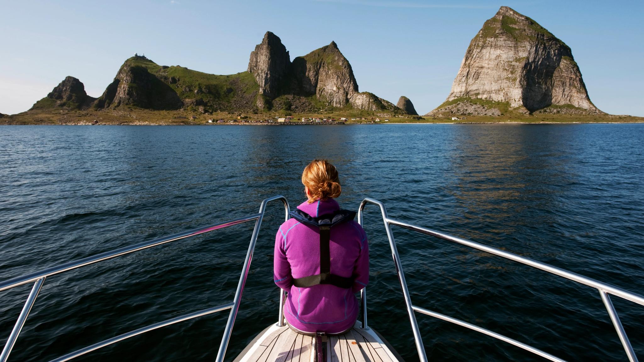 A woman sitting at the tip of a boat, looking out towards the mountains of Træna in Helgeland, Northern Norway.