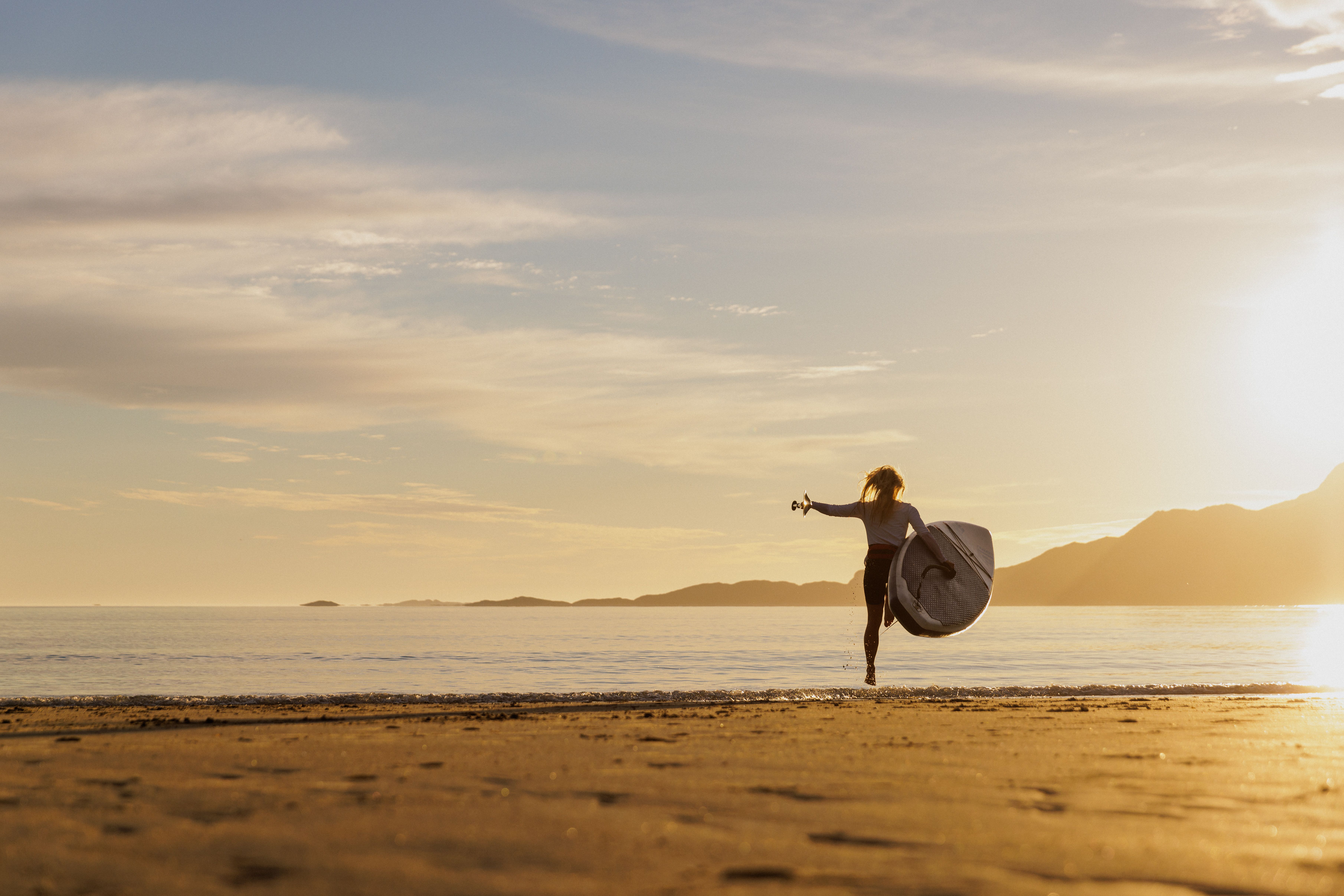 A woman going out in the water with a paddle board in the midnight sun, Northern Norway.