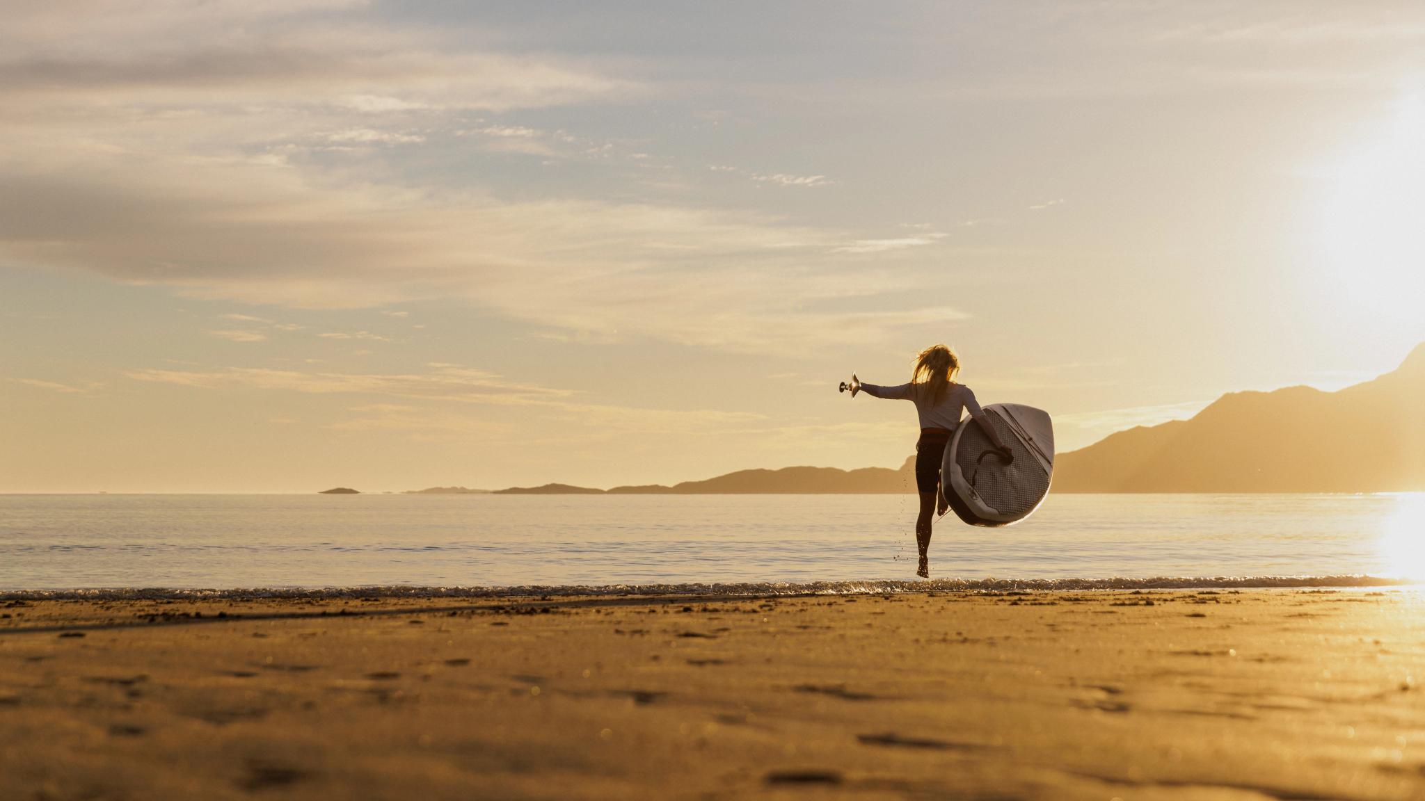 A woman going out in the water with a paddle board in the midnight sun, Northern Norway.