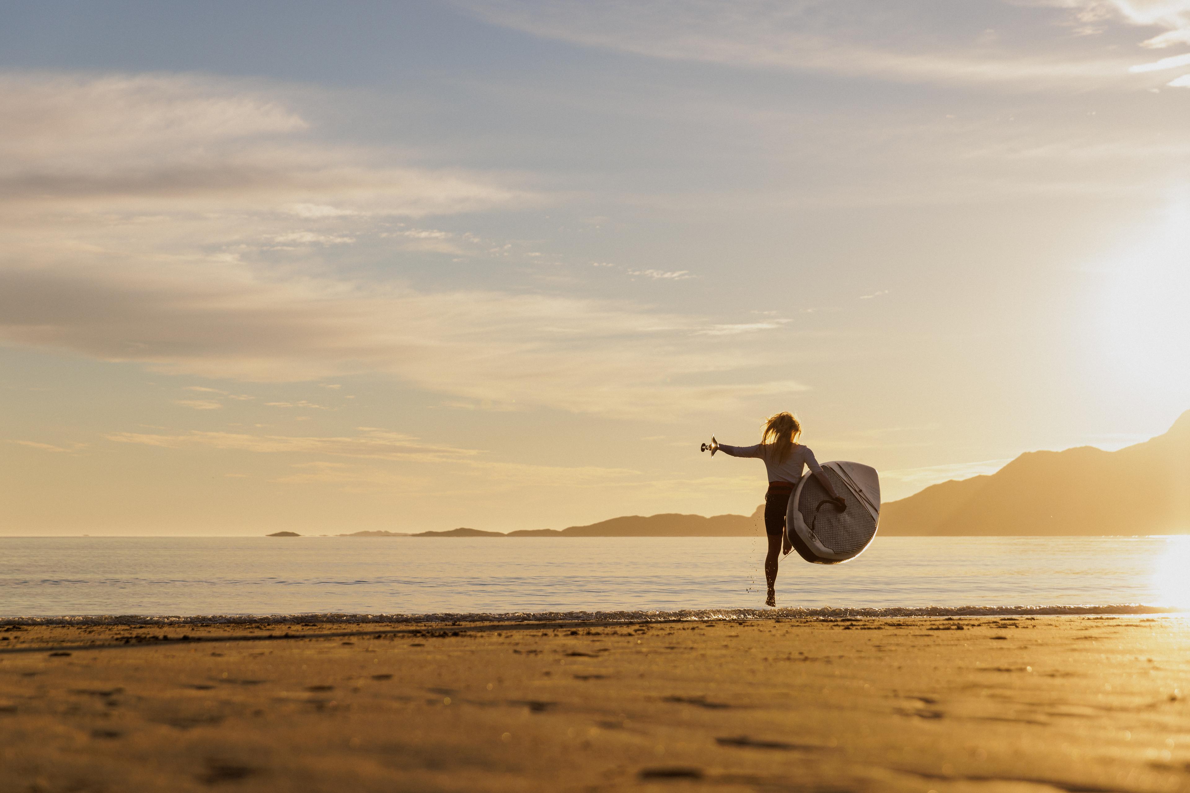 A woman going out in the water with a paddle board in the midnight sun, Northern Norway.