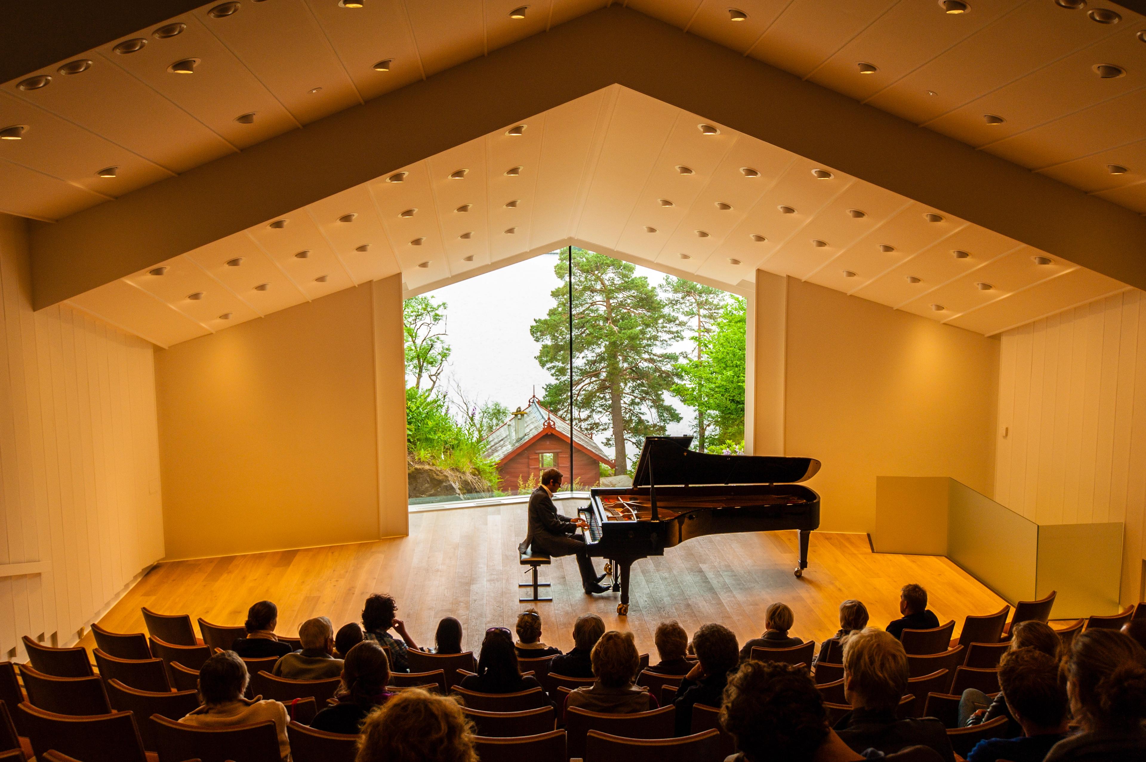 Man playing the piano in front of an audience at the Troldsalen room at Edvard Grieg Museum Troldhaugen in Bergen, Norway