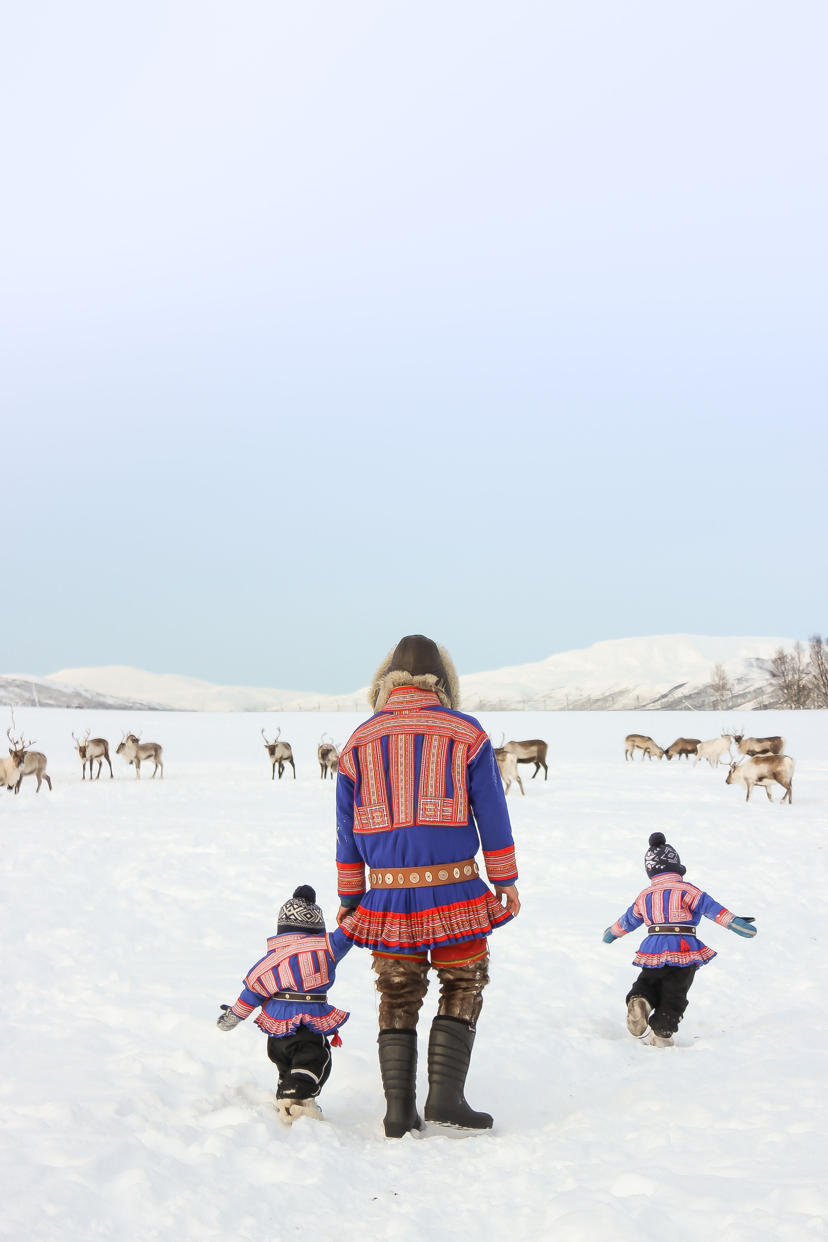 Sami children and their father wearing kofter in the snow