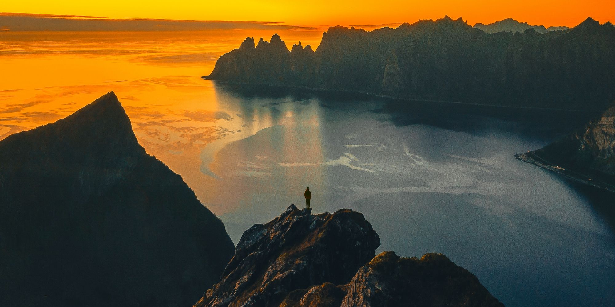 A man standing on the tip of a mountain in the midnight sun at Senja