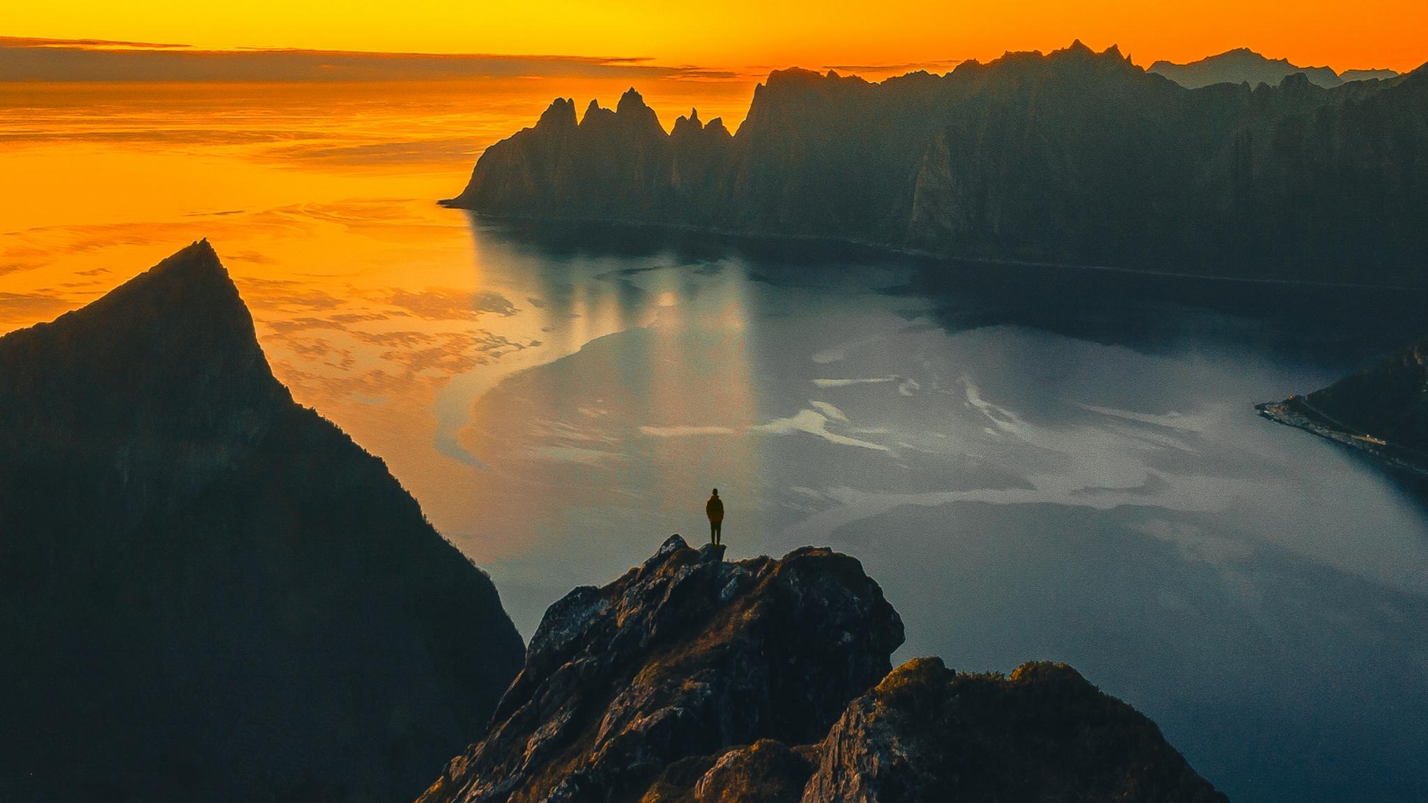 A man standing on the tip of a mountain in the midnight sun at Senja