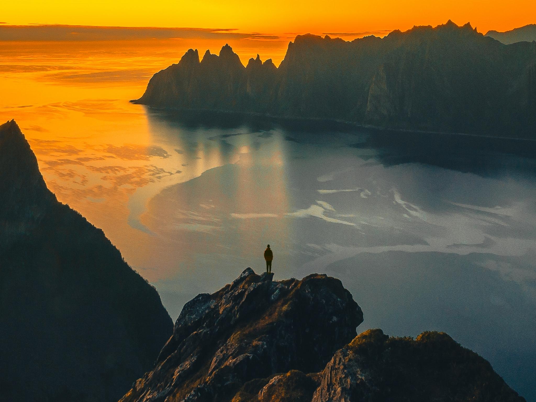 A man standing on the tip of a mountain in the midnight sun at Senja