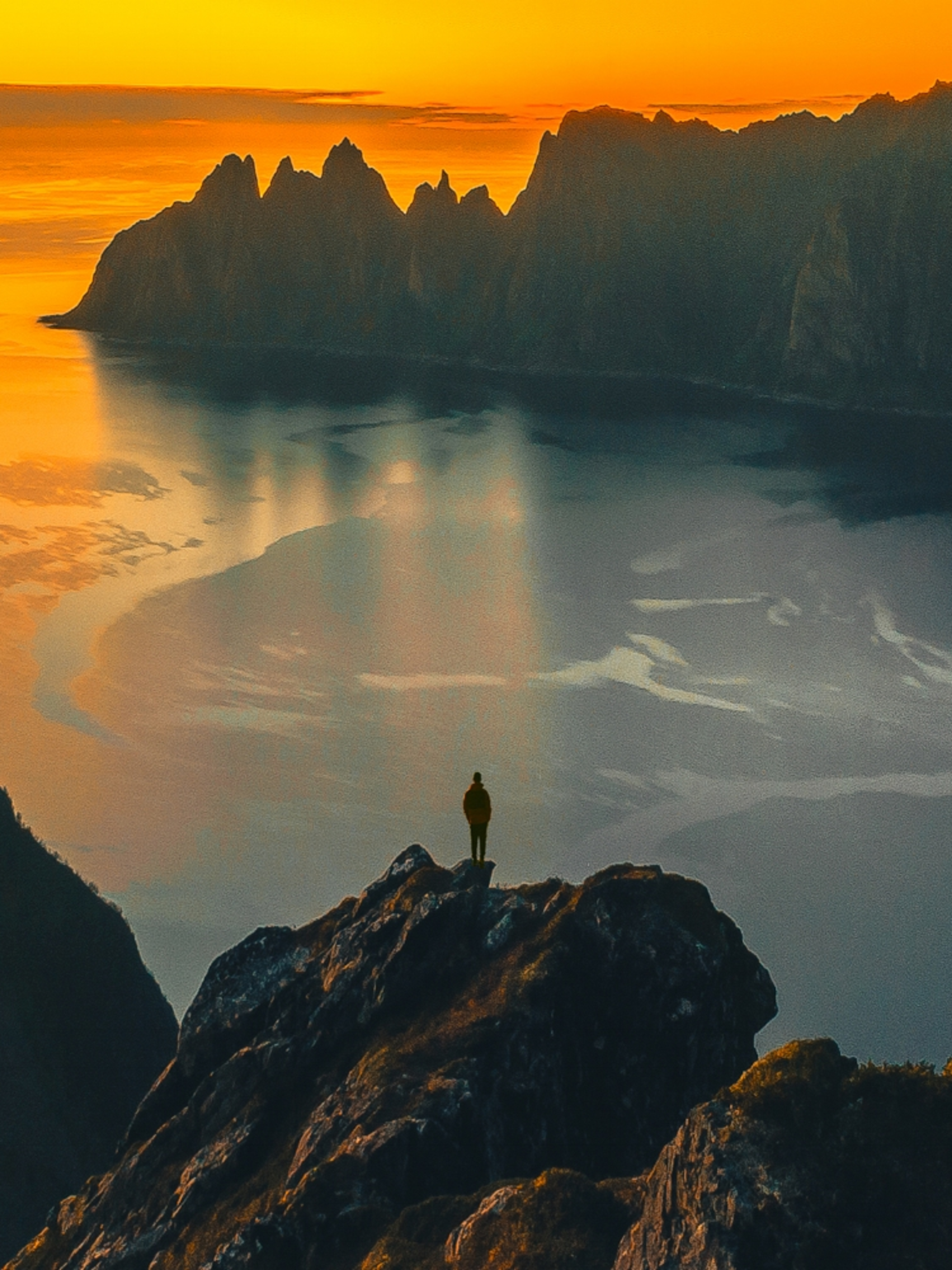 A man standing on the tip of a mountain in the midnight sun at Senja