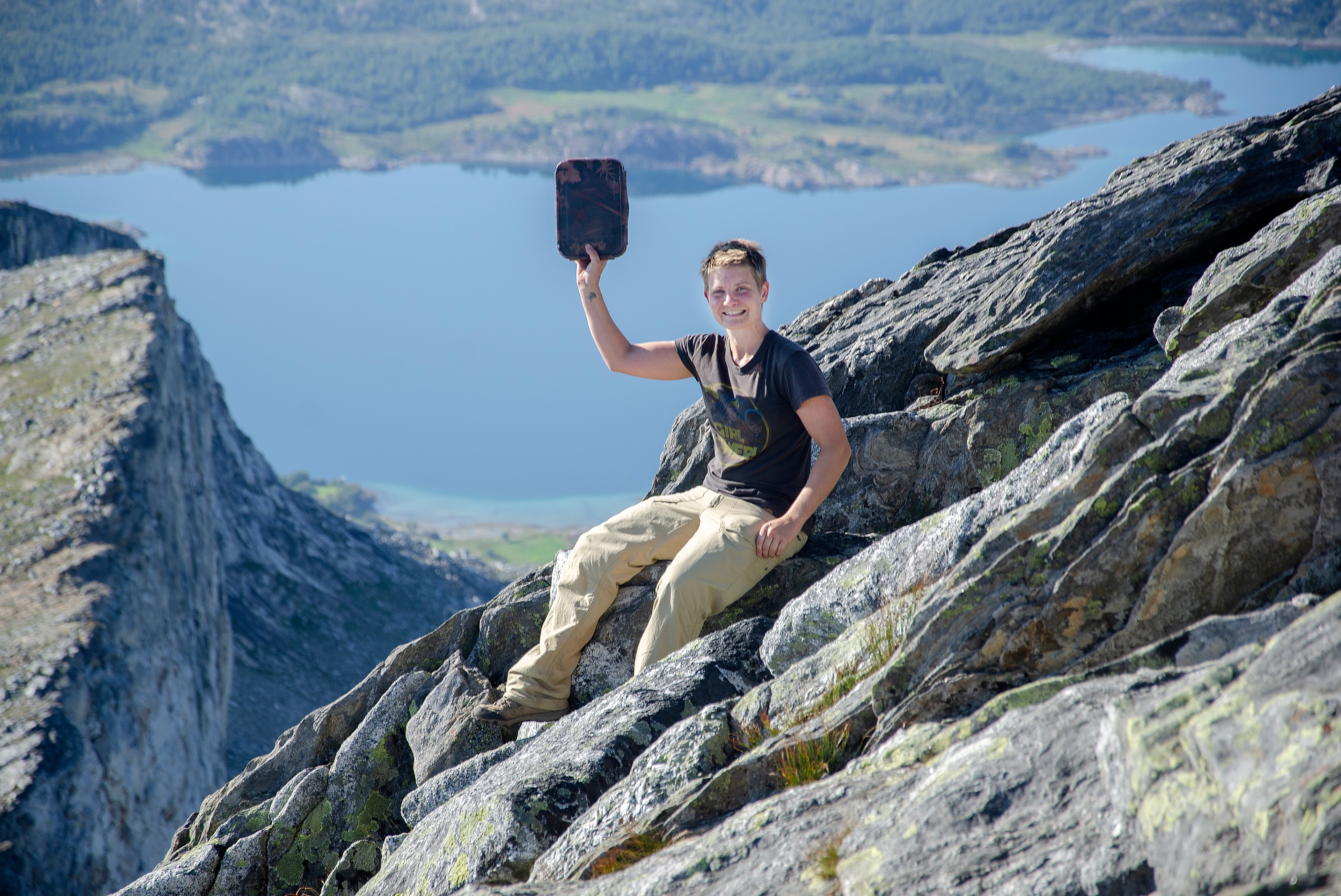A woman sitting on a rock with a fjord in the background while geocaching at the mountain massif Børvasstindan close to Bodø in Northern Norway