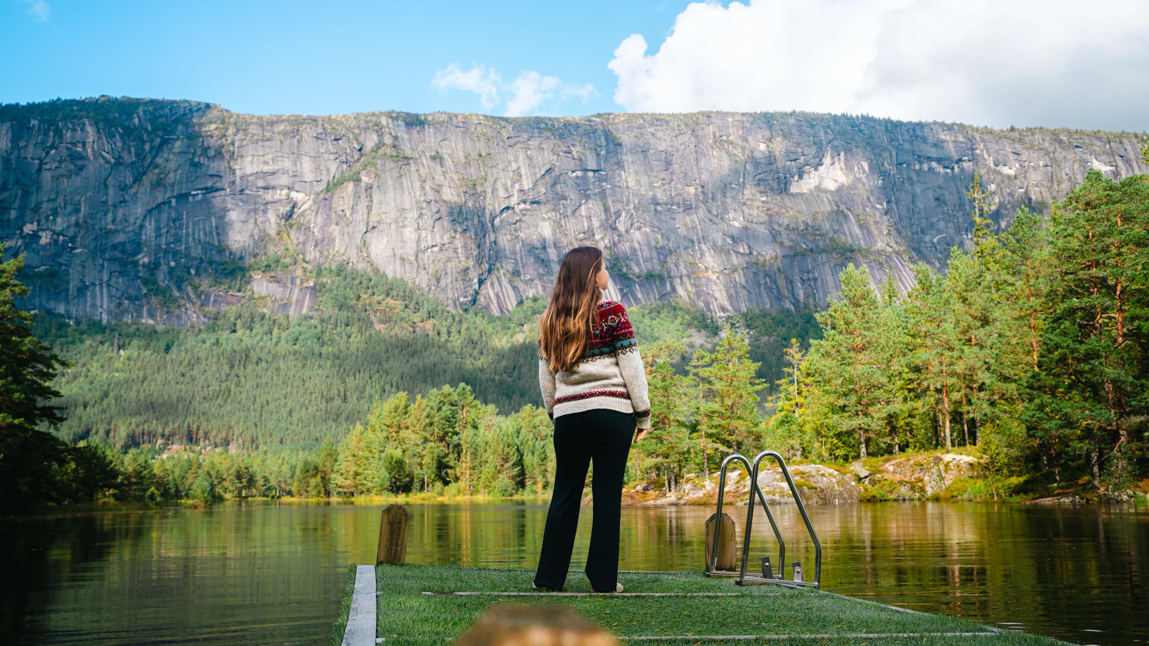 A woman standing by the river Otra, with a stunning mountain backdrop in the Setesdal Valley.