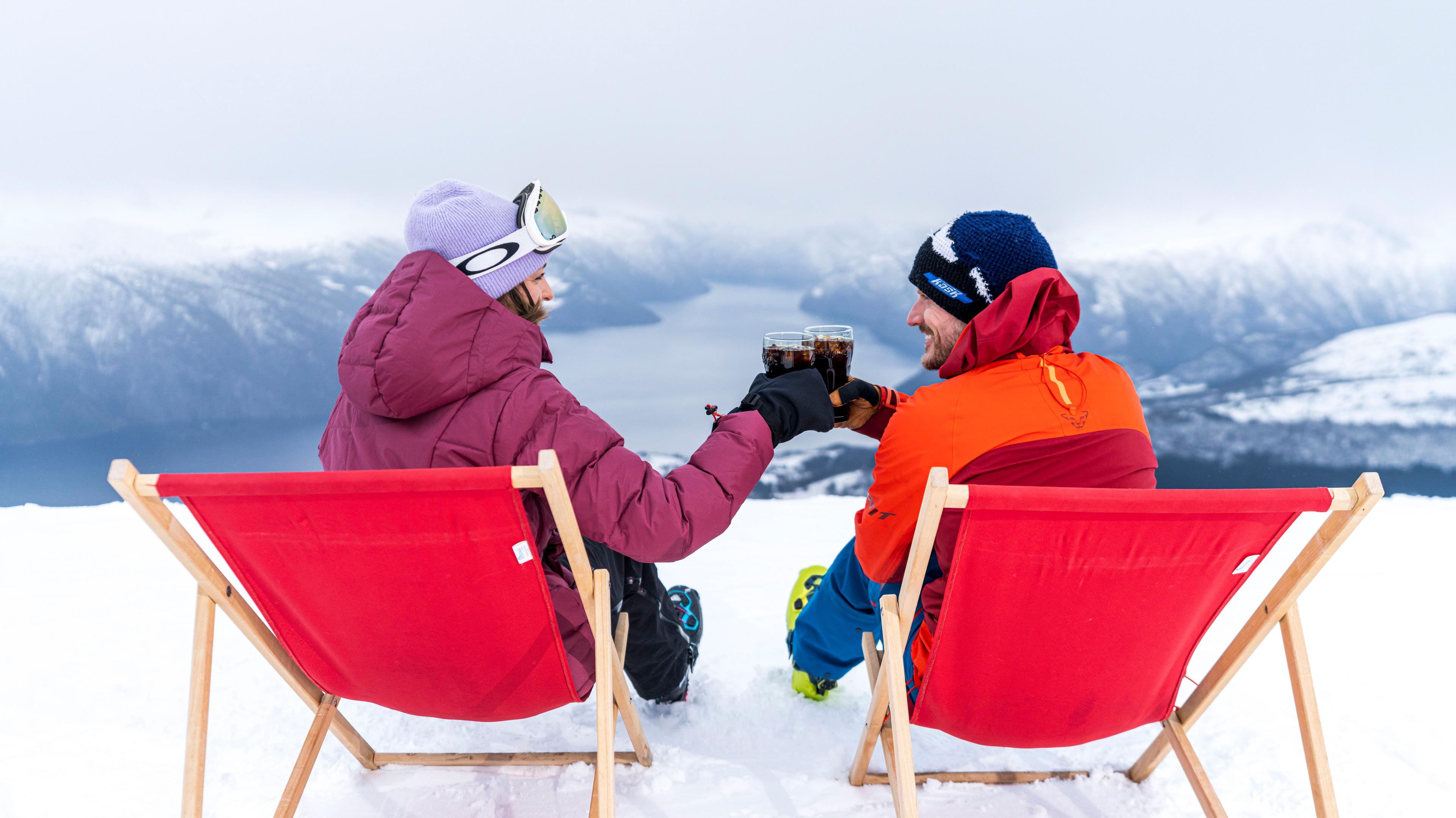 Two people toasting in sun chairs by the Fjord Panorama restaurant at Strandafjellet