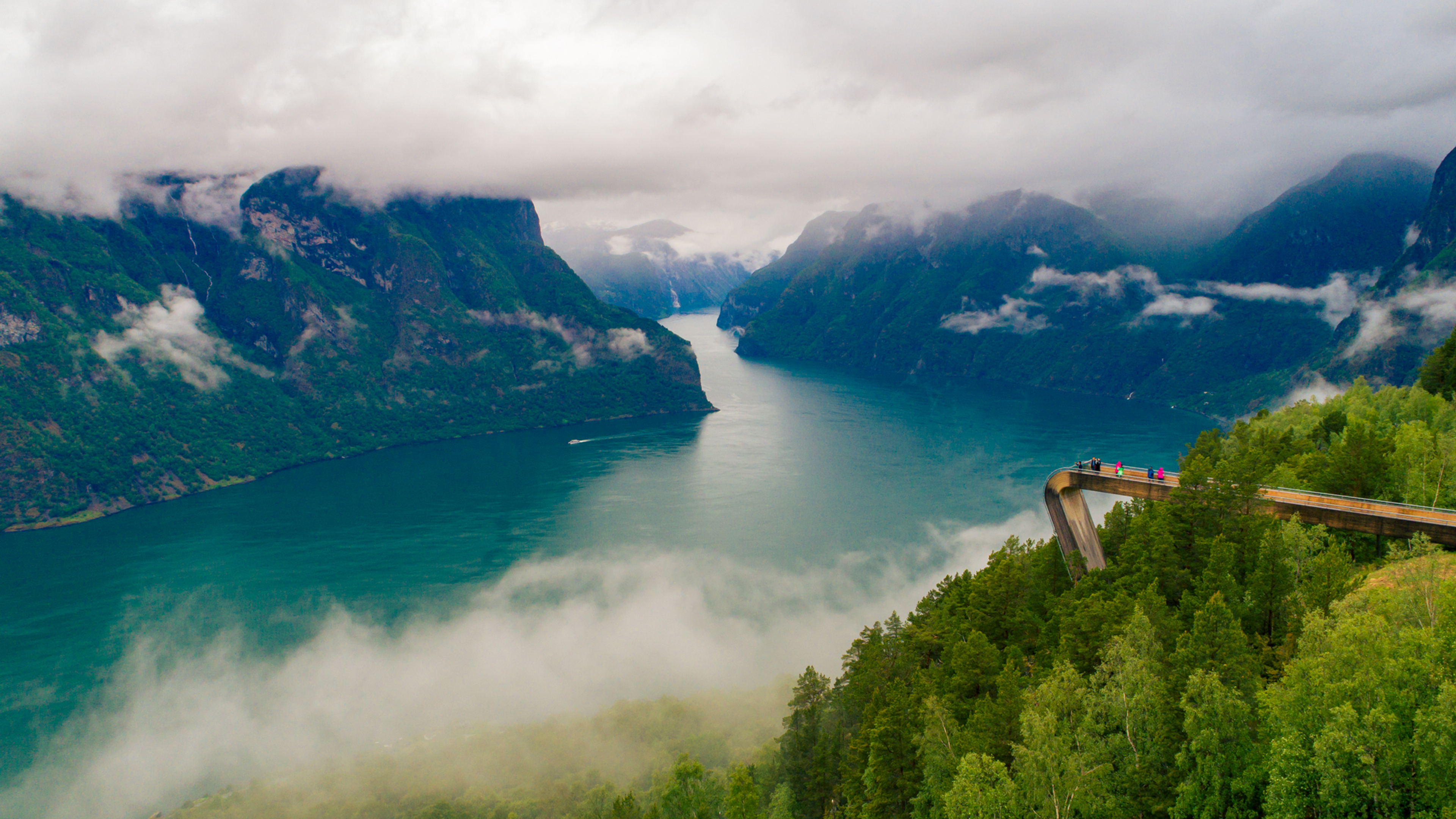 People on a bridge viewpoint overlooking the fjord and snowcapped mountains