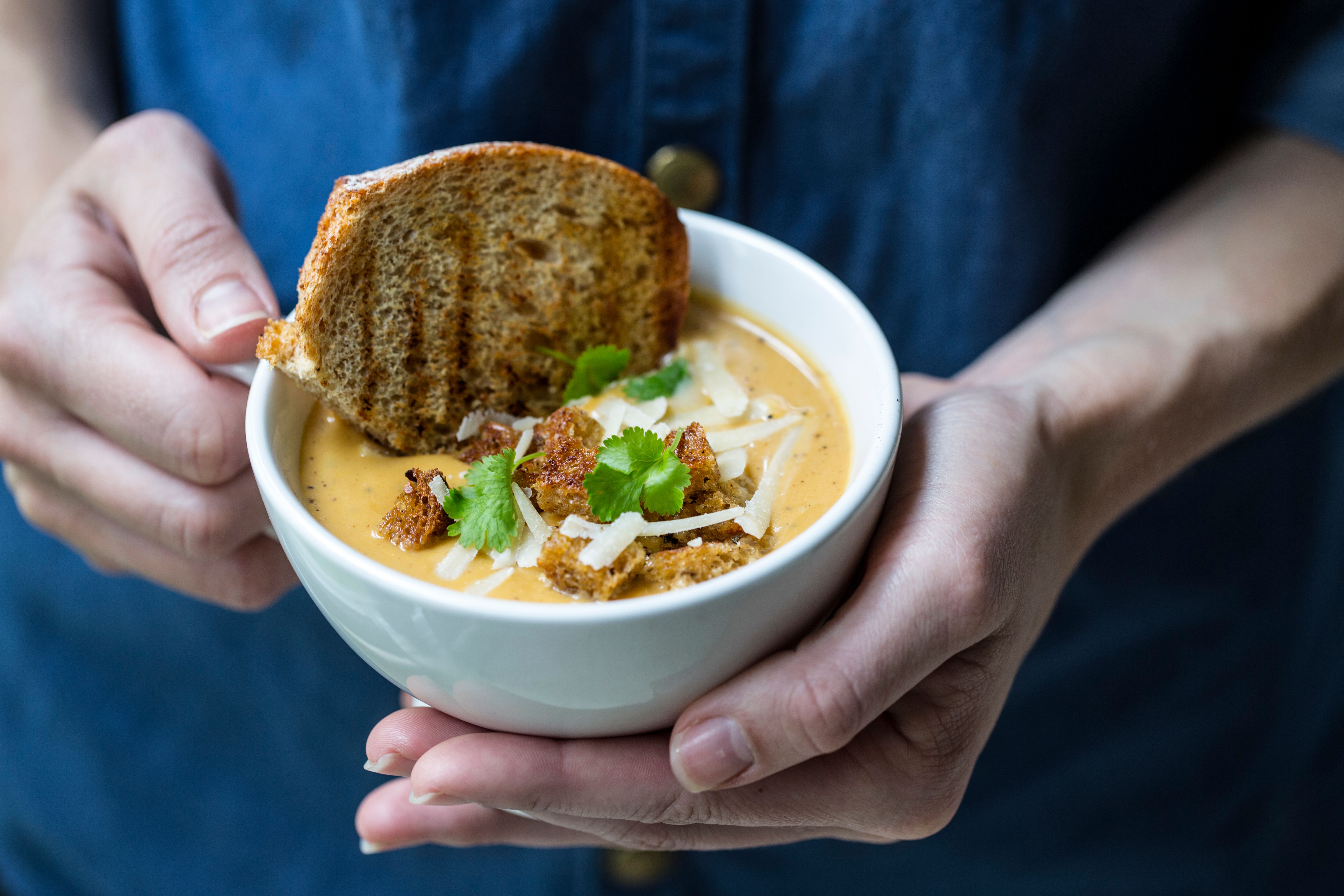 A person holding up a bowl of pumpkin soup served with croutons and toasted bread in Norway
