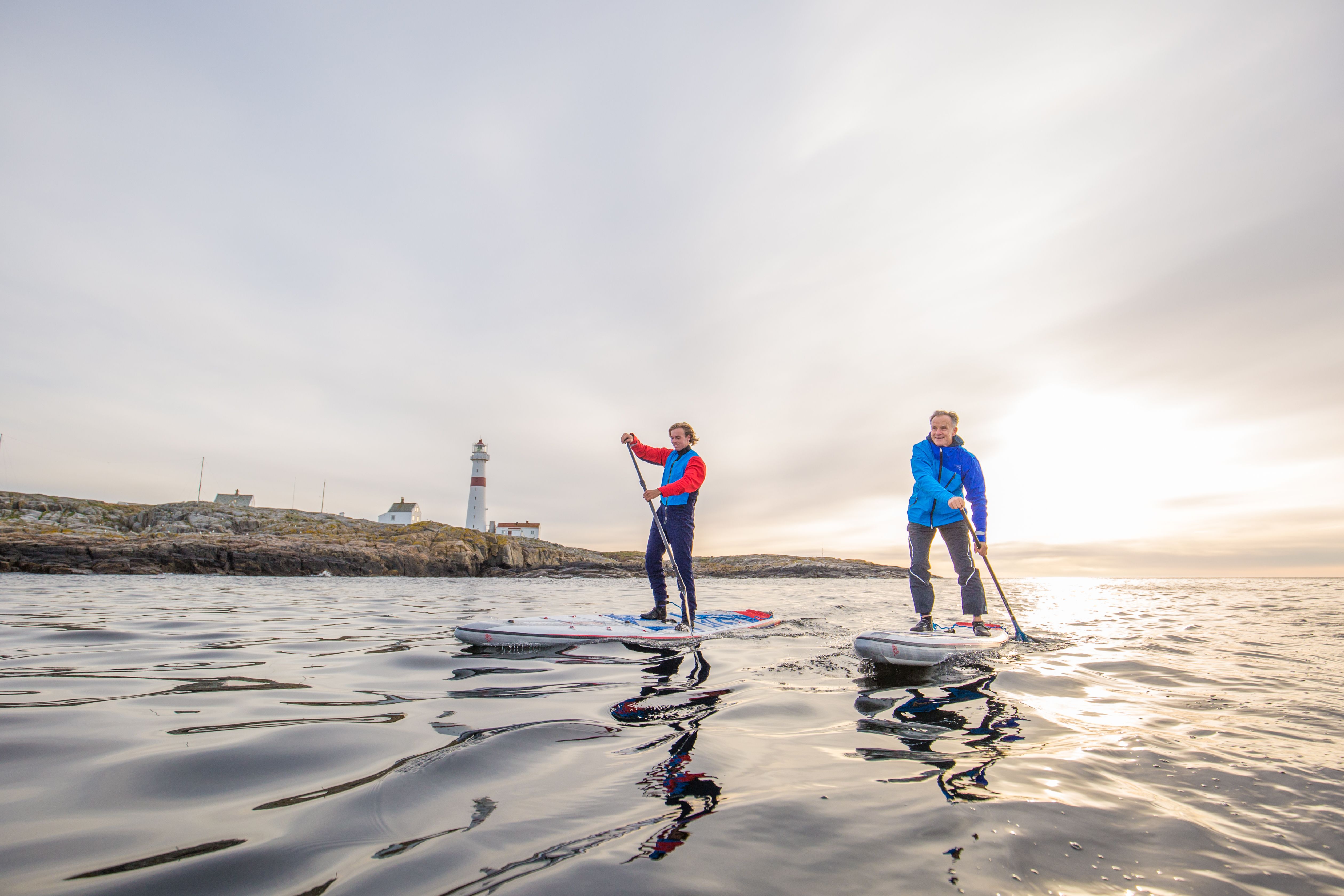 Two people stand up paddleboarding in Arendal, Southern Norway, with Torungen lighthouse in the background.