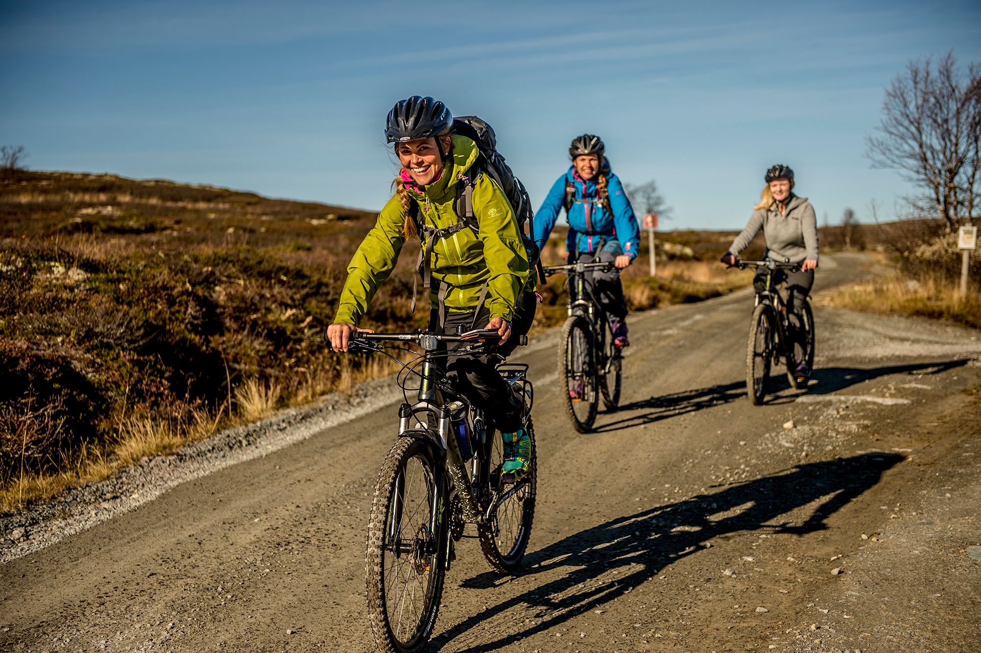 Three people cycling at a dirt road on the Hardangervidda mountain plateau in Norway