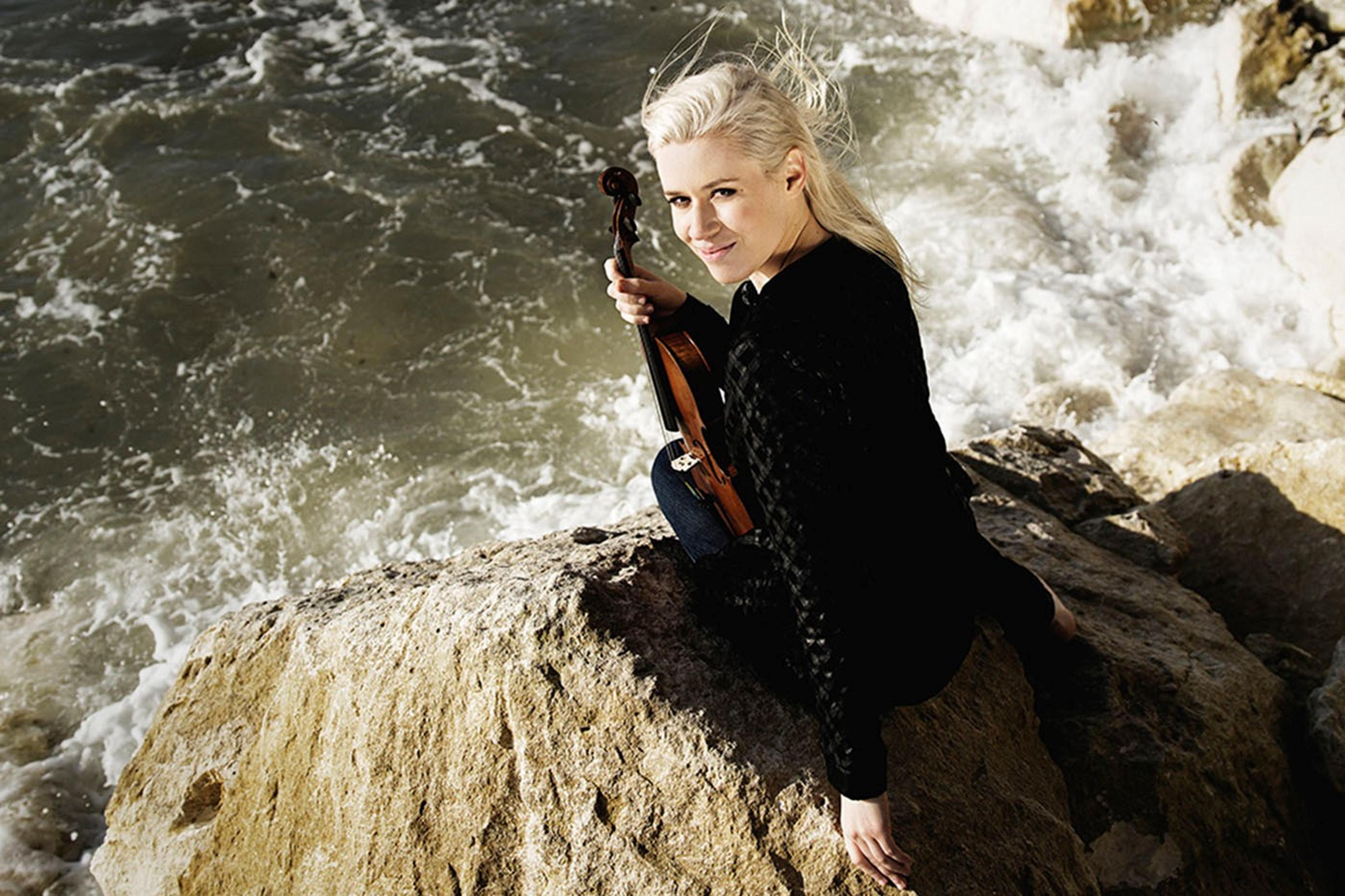 Eldbjørg Hemsing sitting on a rock near the river with her violin