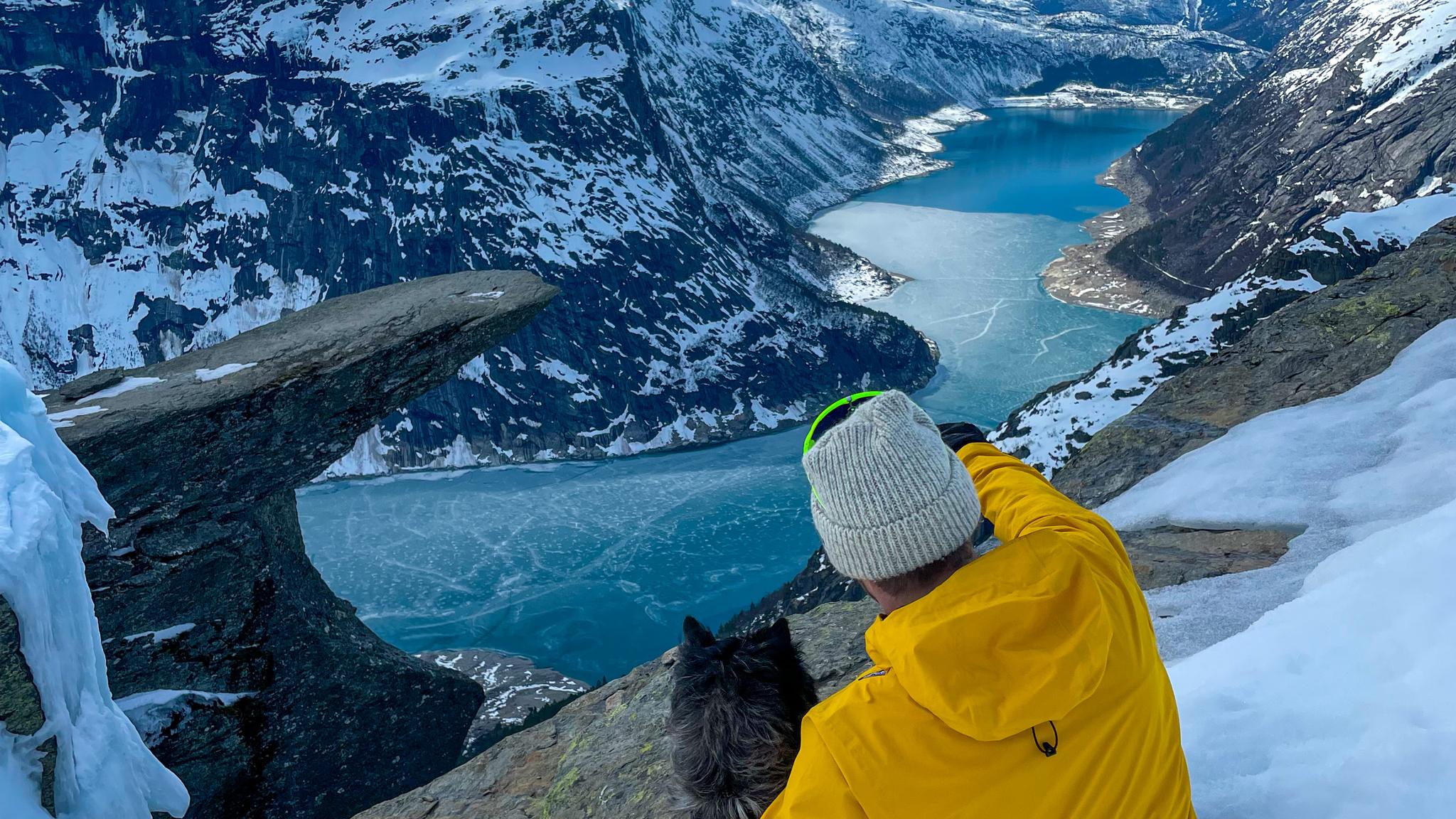 A man and a dog looking at the Trolltunga mountain formation in winter.
