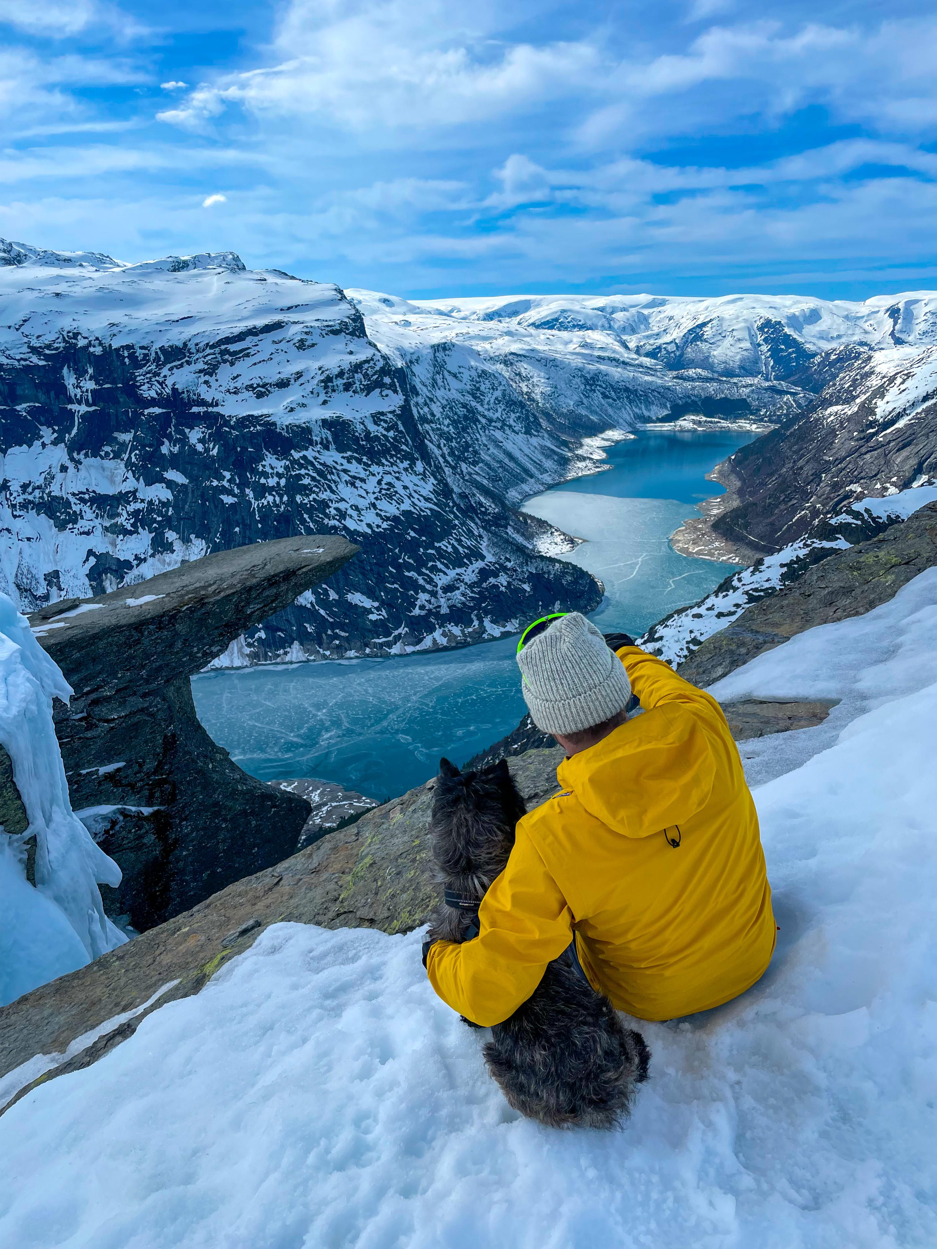 A man and a dog looking at the Trolltunga mountain formation in winter.