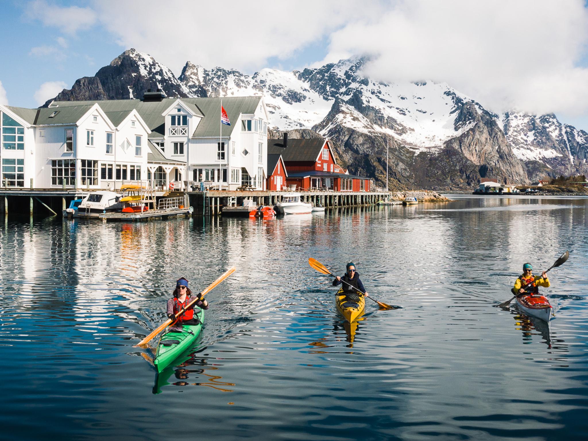 People winter kayaking by the Henningsvær Bryggehotell in Lofoten, Northern Norway.
