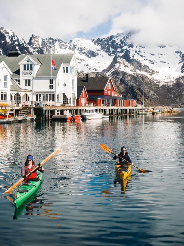 People winter kayaking by the Henningsvær Bryggehotell in Lofoten, Northern Norway.