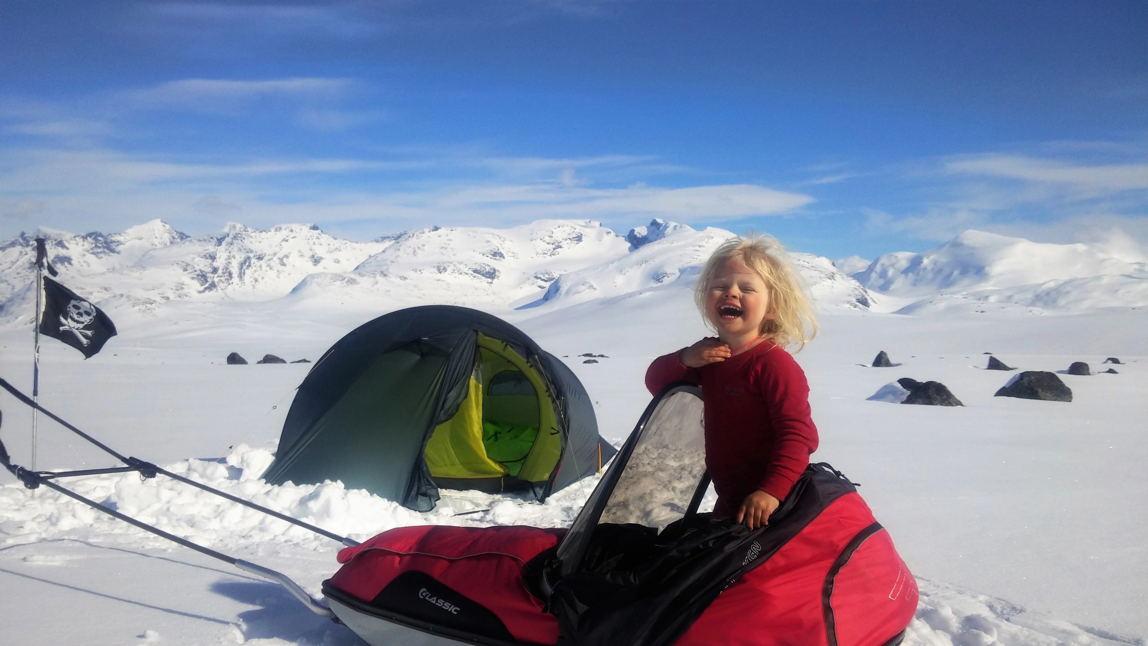 En ung jente står i en skipulk og smiler på en solfylt vinterdag i Jotunheimen nasjonalpark
