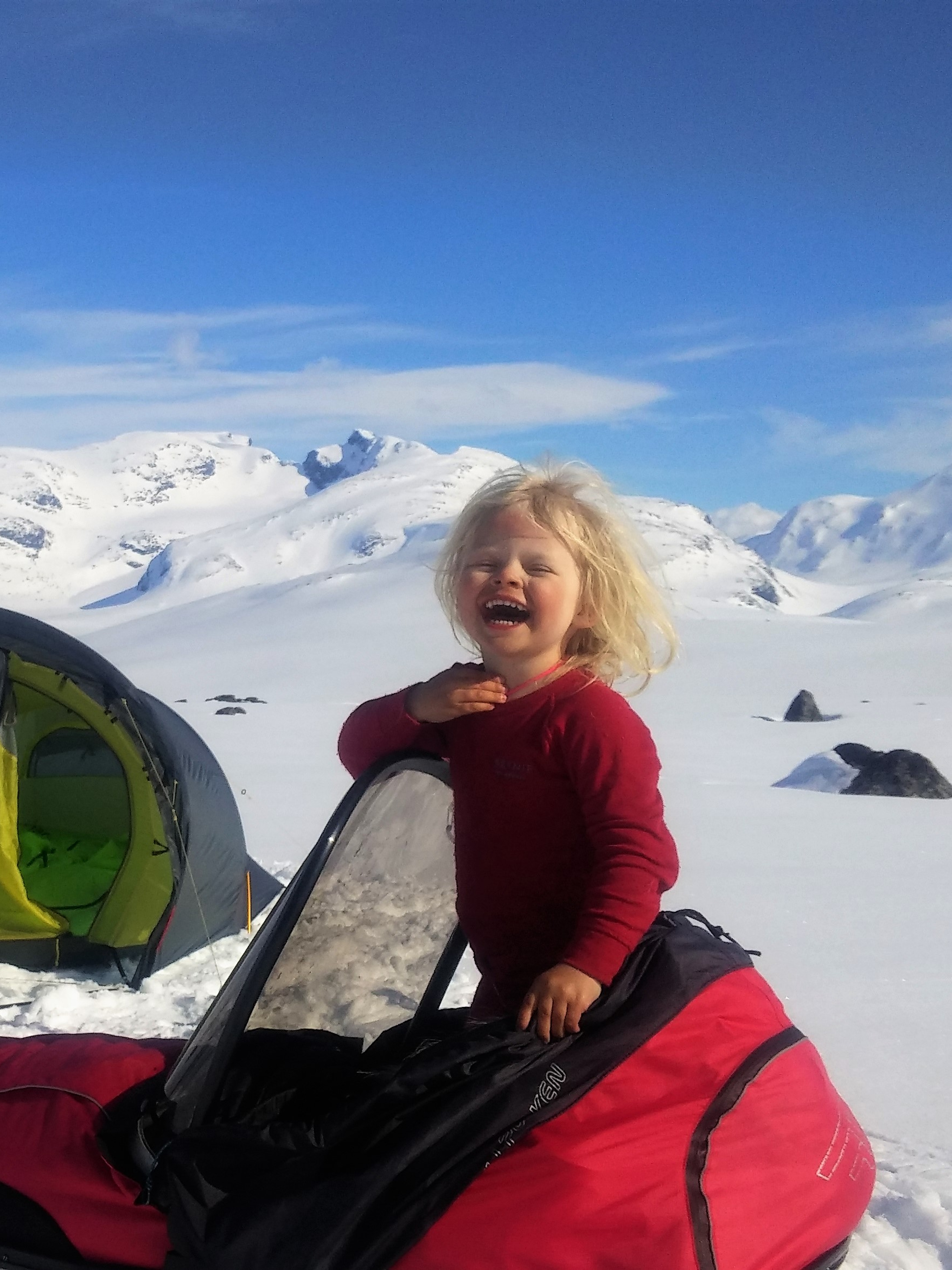The 4-year-old Mina standing in a ski pulk in front of a tent on a sunny winter day in Jotunheimen national park, Eastern Norway