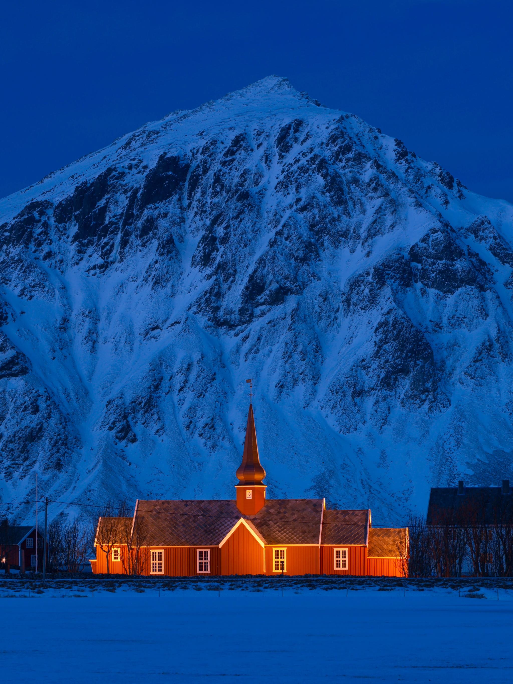 A lit up church in front of a steep mountain.