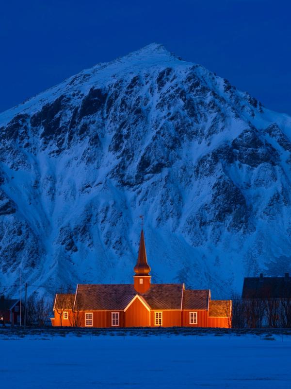 A lit up church in front of a steep mountain.