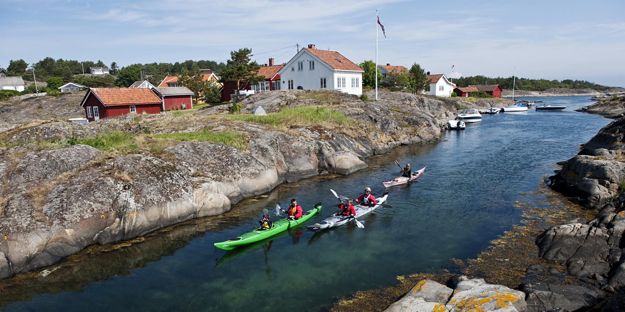 En familie padler i kajakker gjennom et sund i Risørskjærgården på Sørlandet