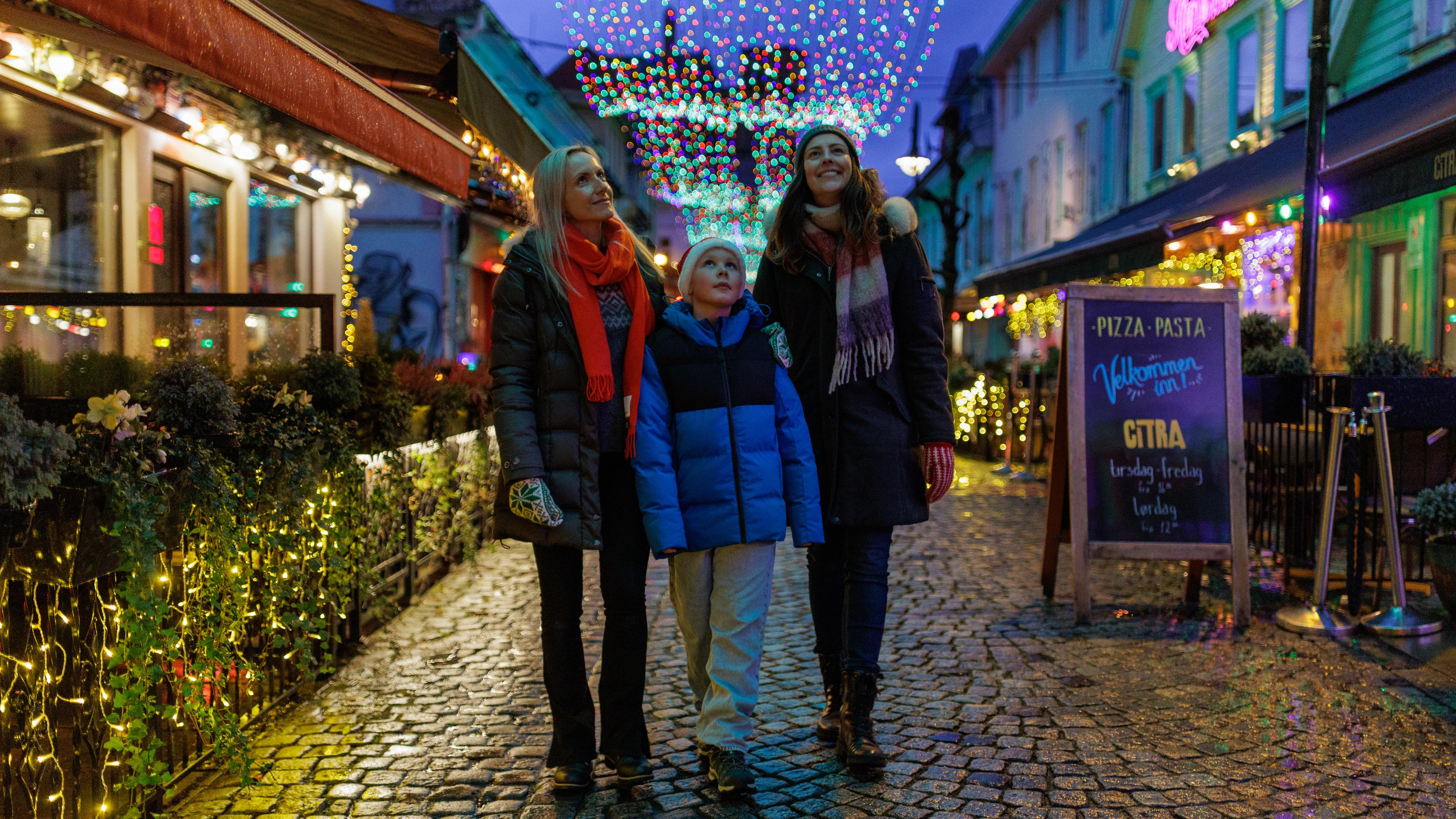 Two woman and a boy strolling down Fargegaten, surrounded by twinkling Christmas lights
