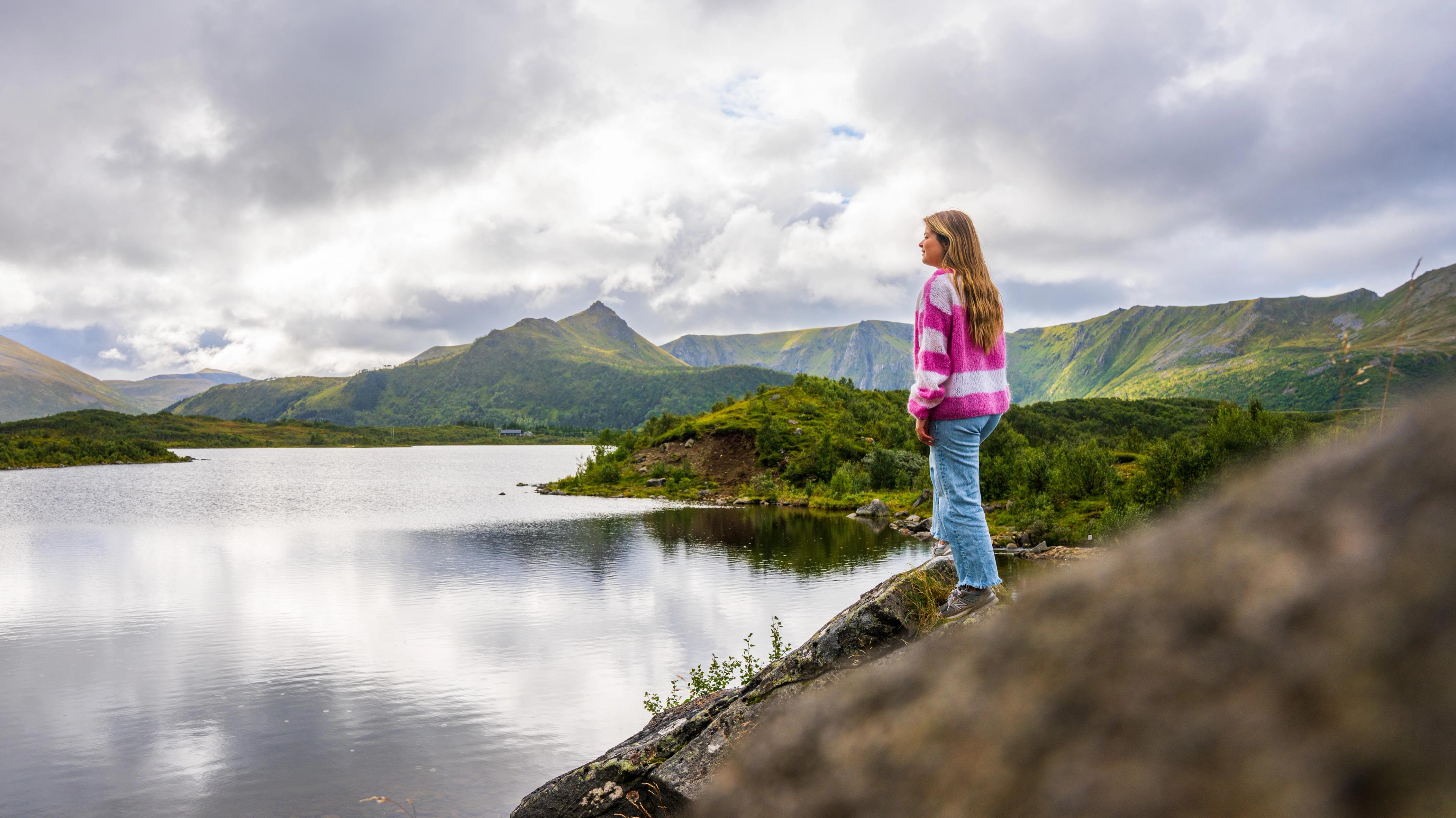 A girl in a pink sweather is looking at a lake at Andøya, Northern Norway