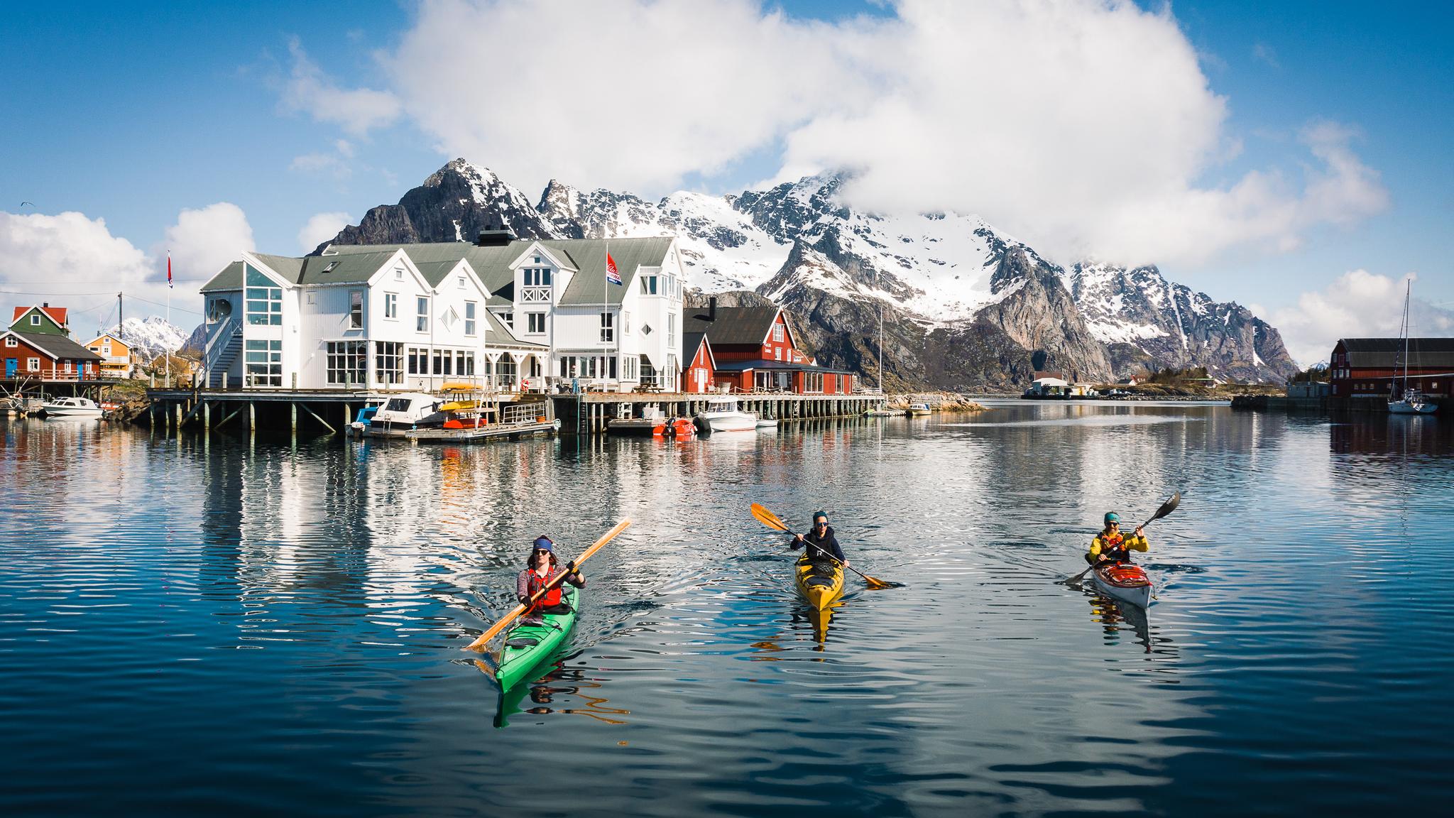 People winter kayaking by the Henningsvær Bryggehotell in Lofoten, Northern Norway.