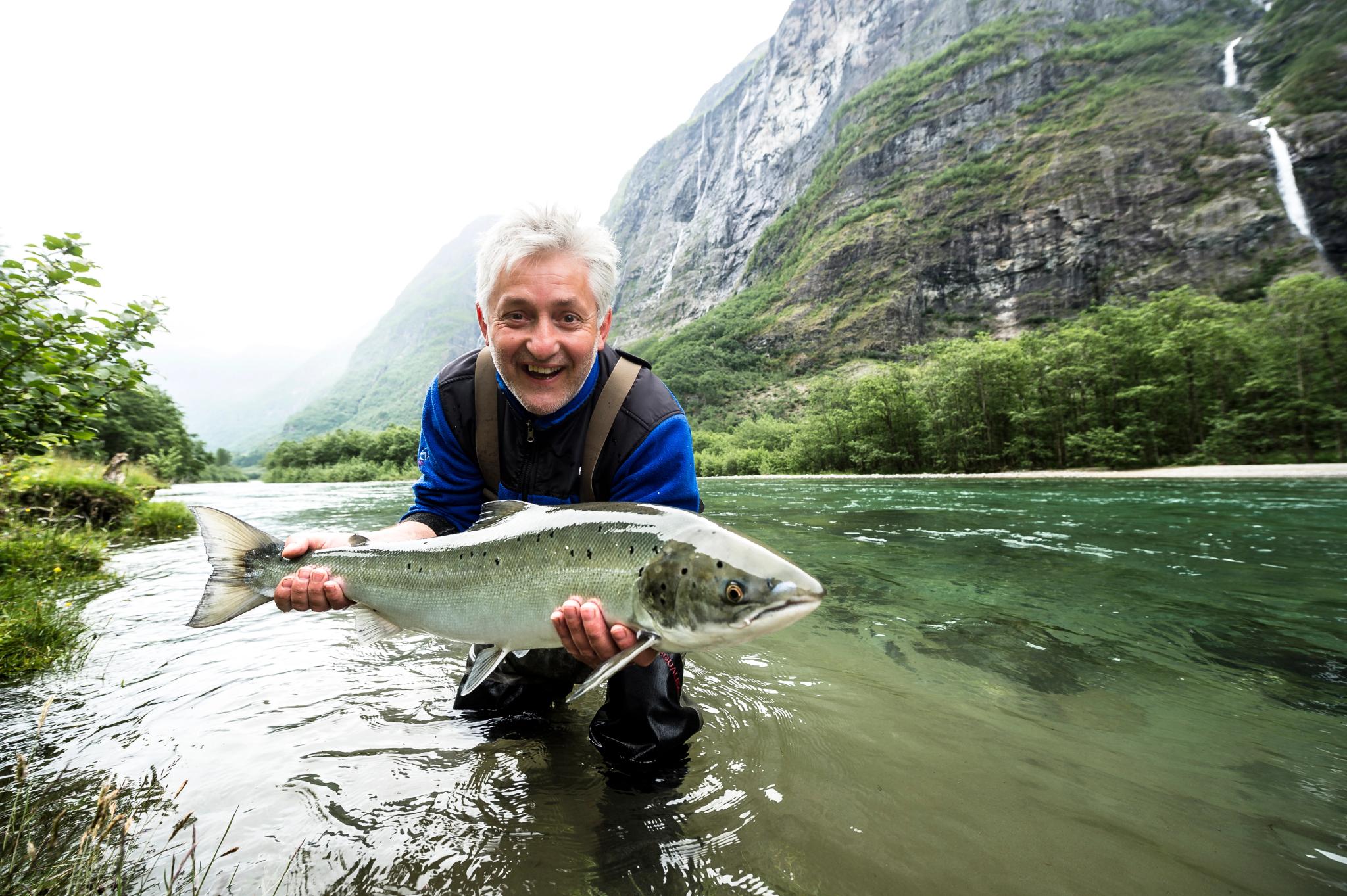 A person standing in Nærøydalselva river in Fjord Norway holding a large salmon