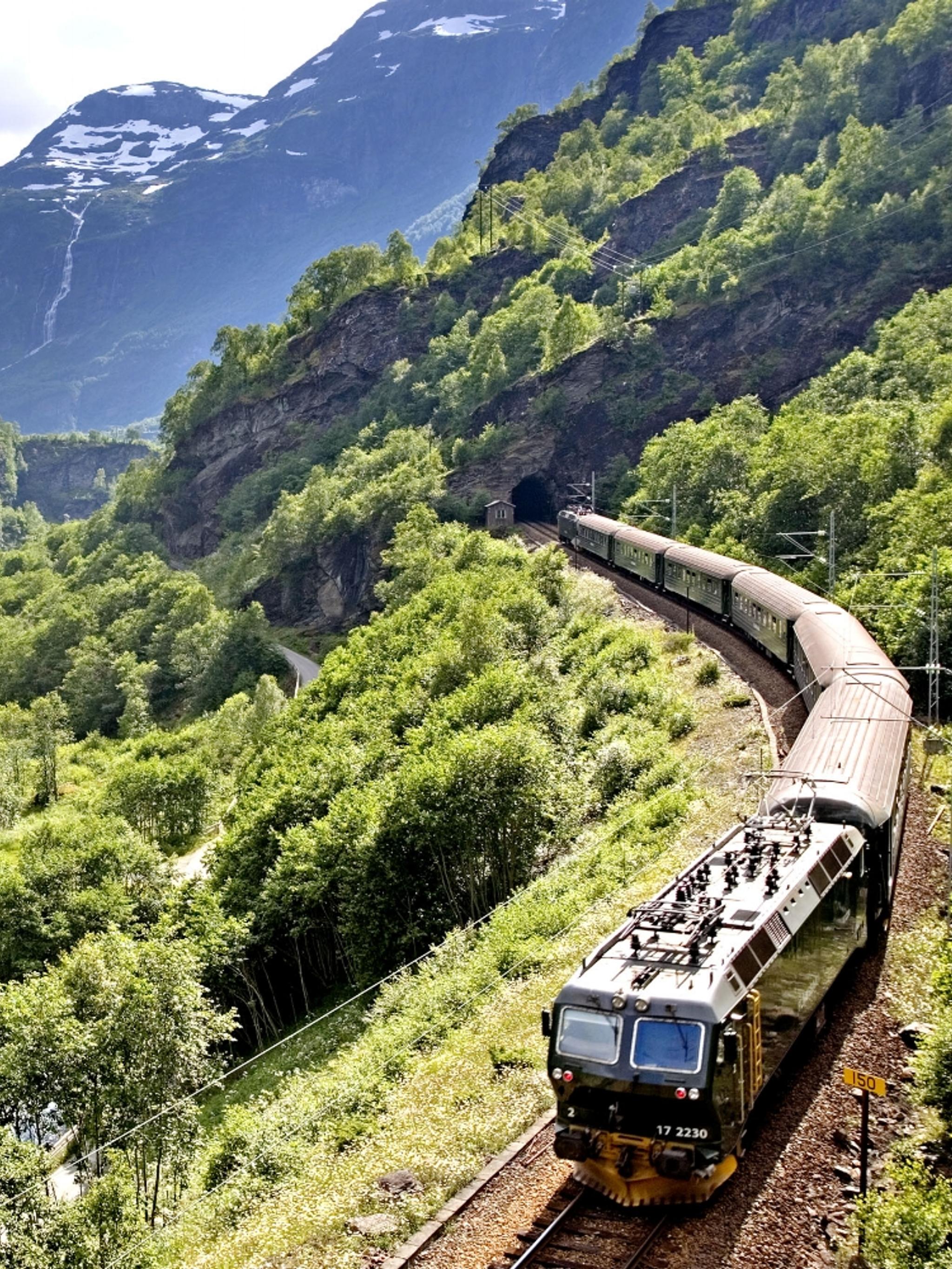 The Flåm Railway going through the landscape of green hills and spectacular mountains in Fjord Norway