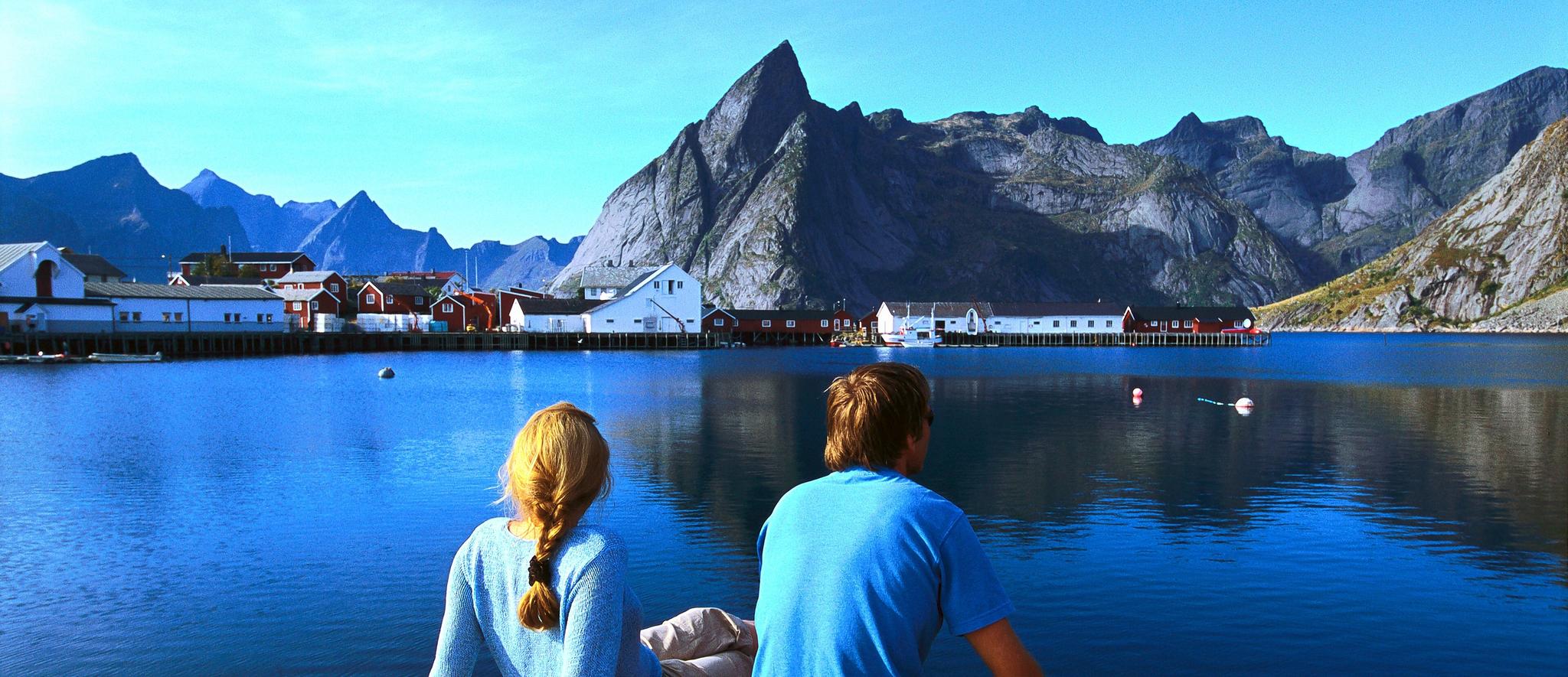 Two people looking out over a fjord towards a fishing village in Lofoten.