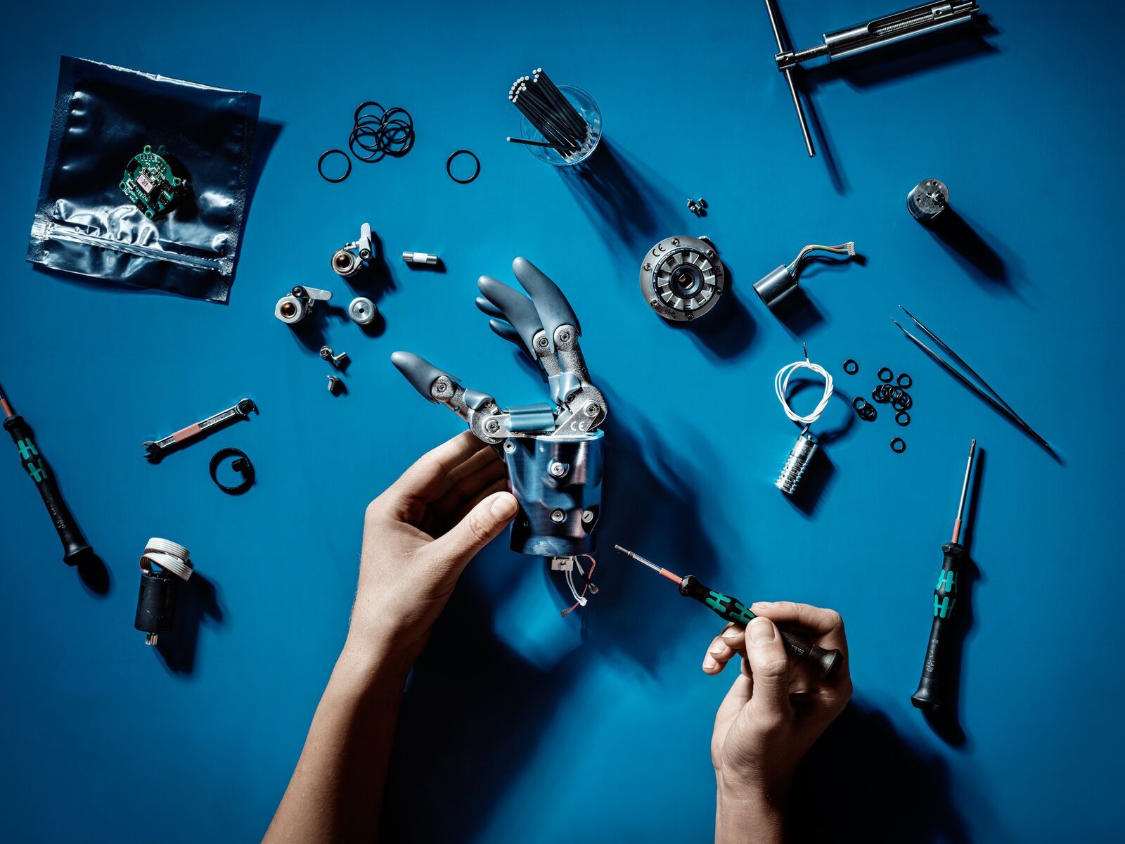 Two hands are working with tools to fix a robot arm