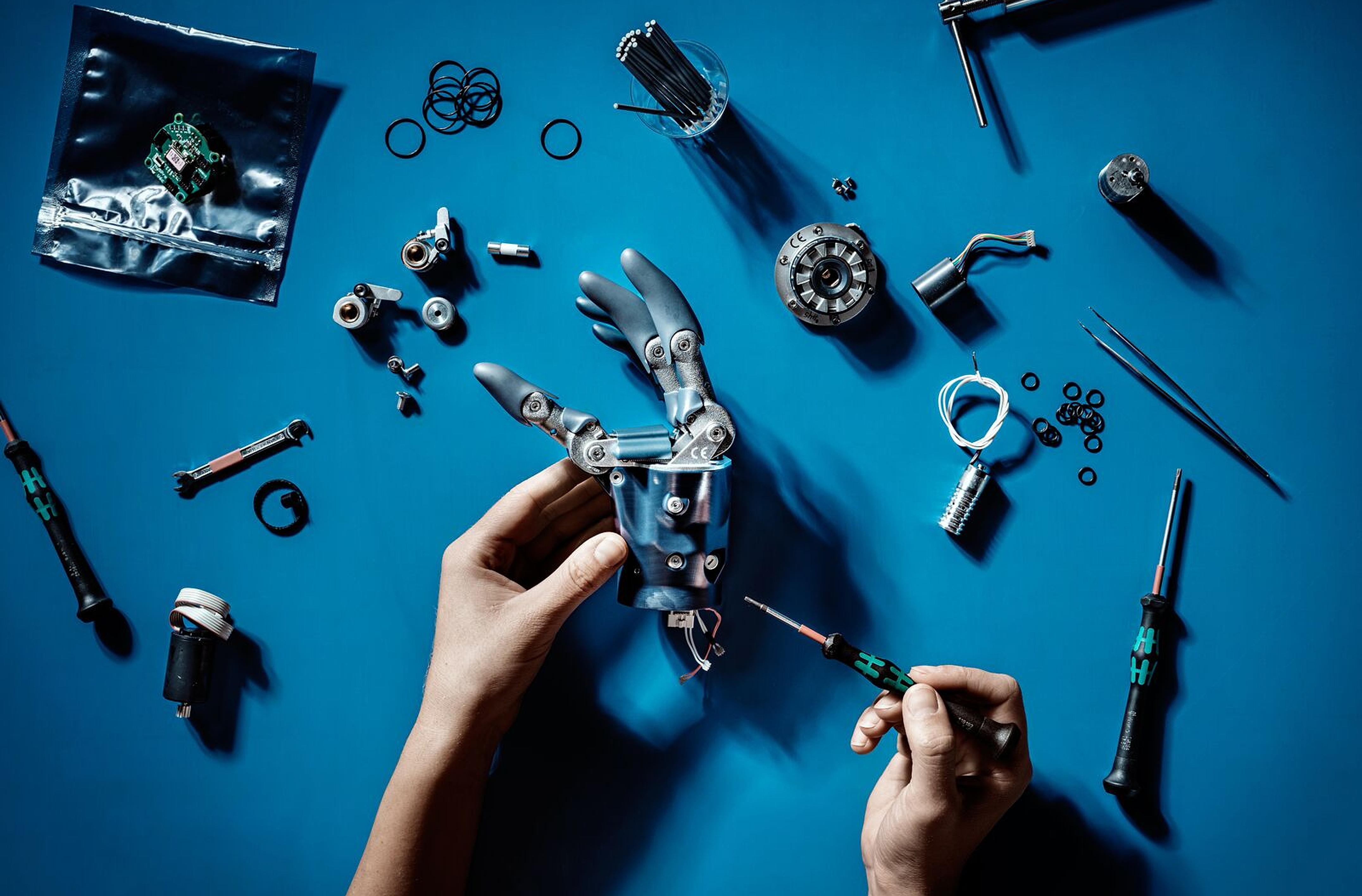 Two hands are working with tools to fix a robot arm