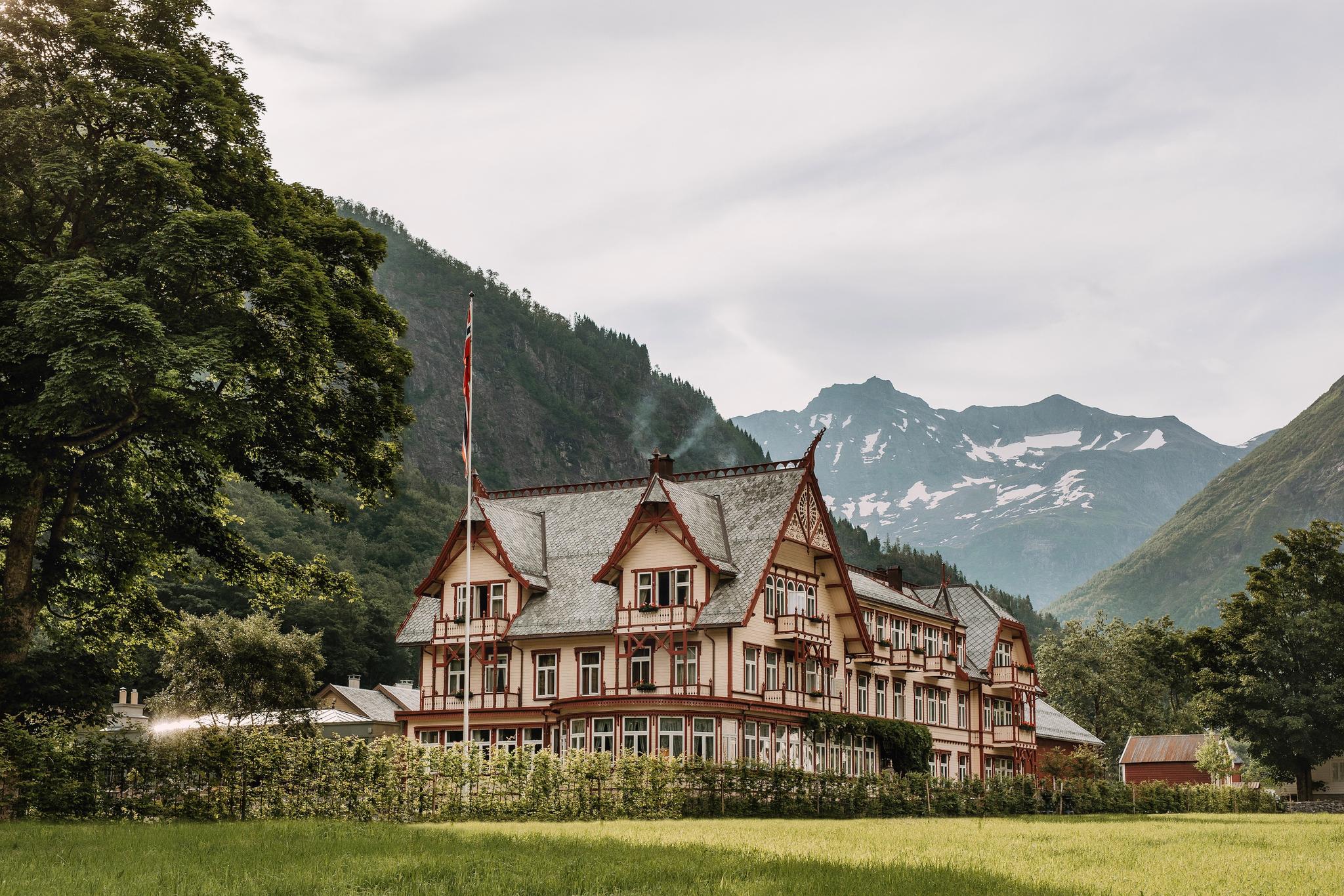 Elegant wooden hotel in mountain valley beneath snow-capped peaks.