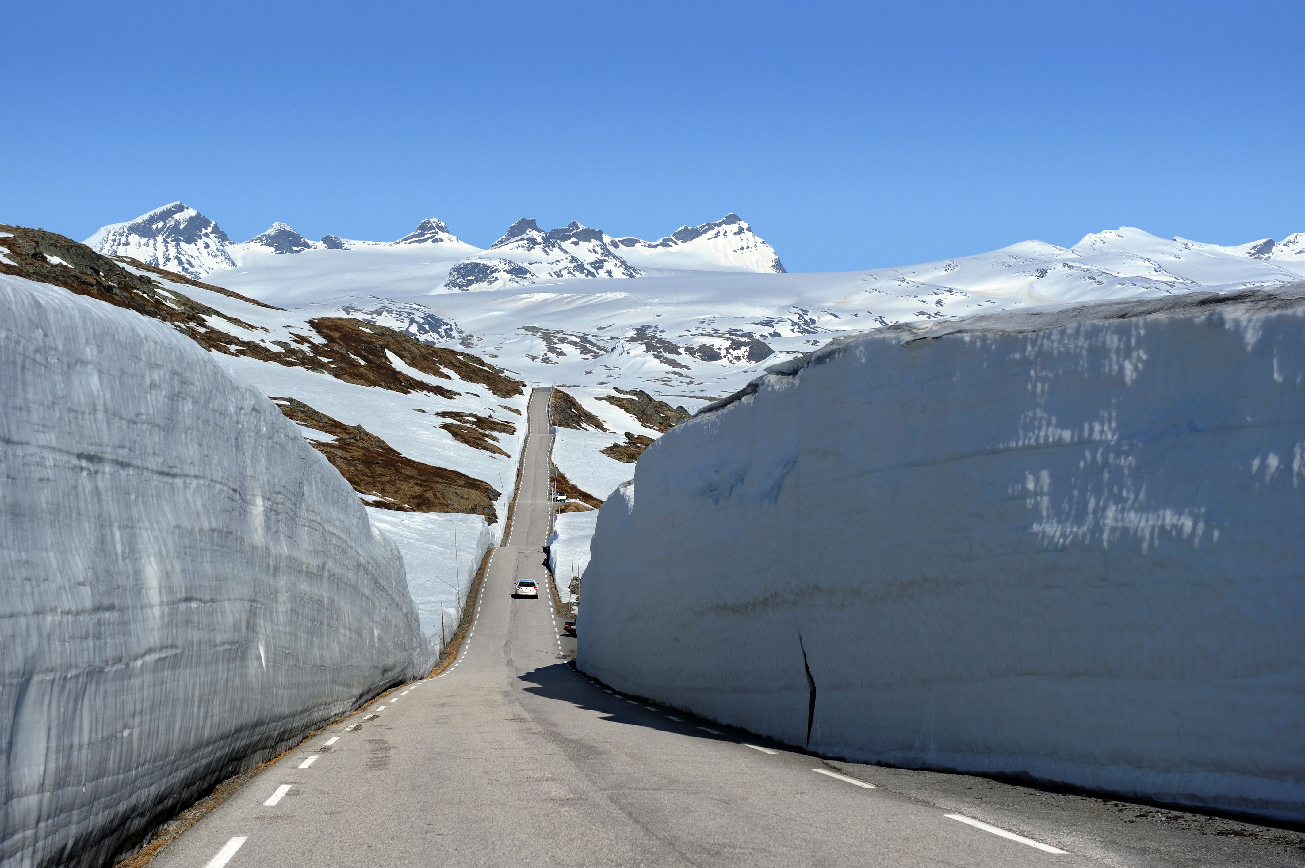 A car between large snow banks on Norwegian Scenic Route Sognefjellet, Fjord Norway