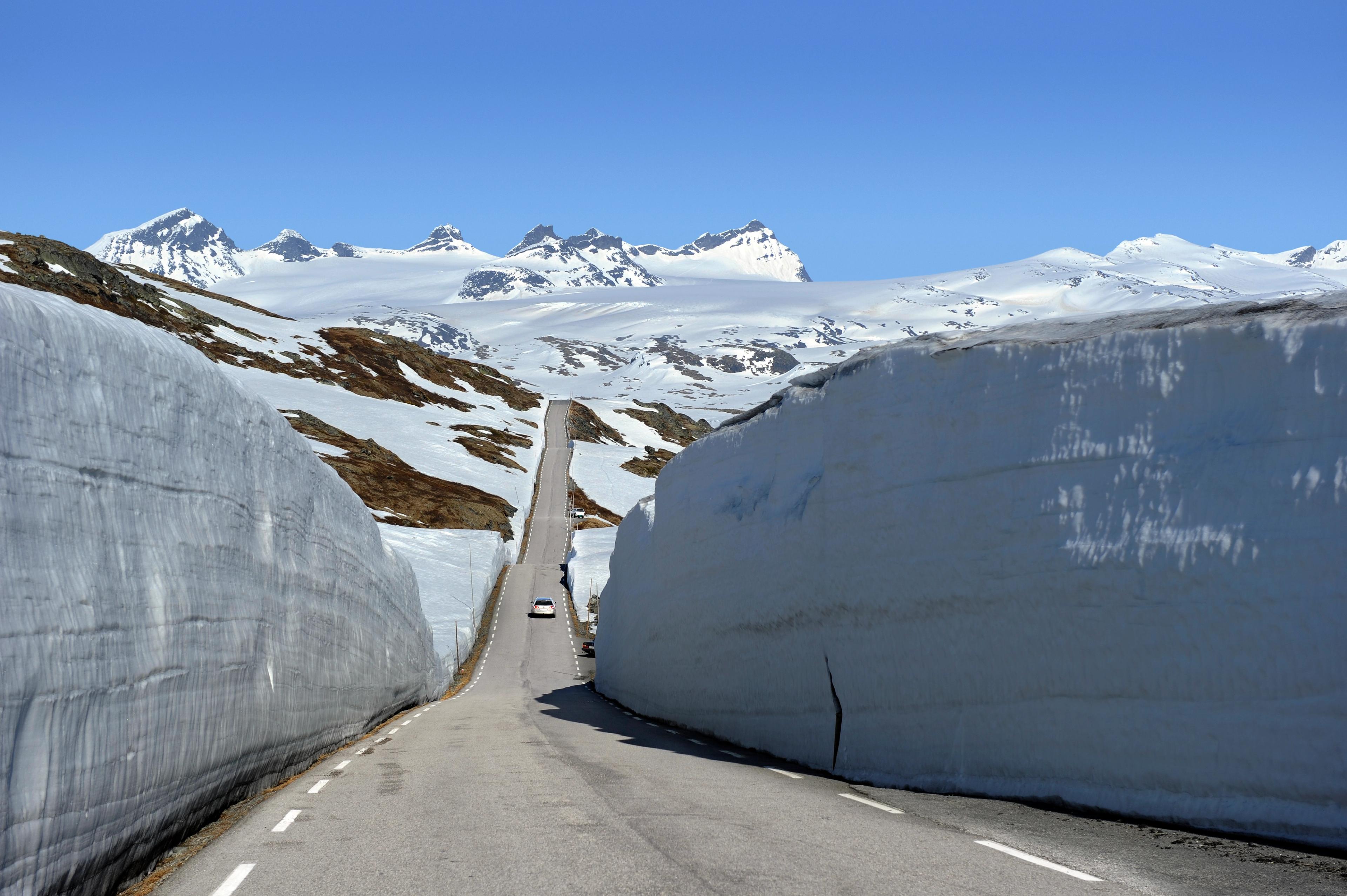 A car between large snow banks on Norwegian Scenic Route Sognefjellet, Fjord Norway