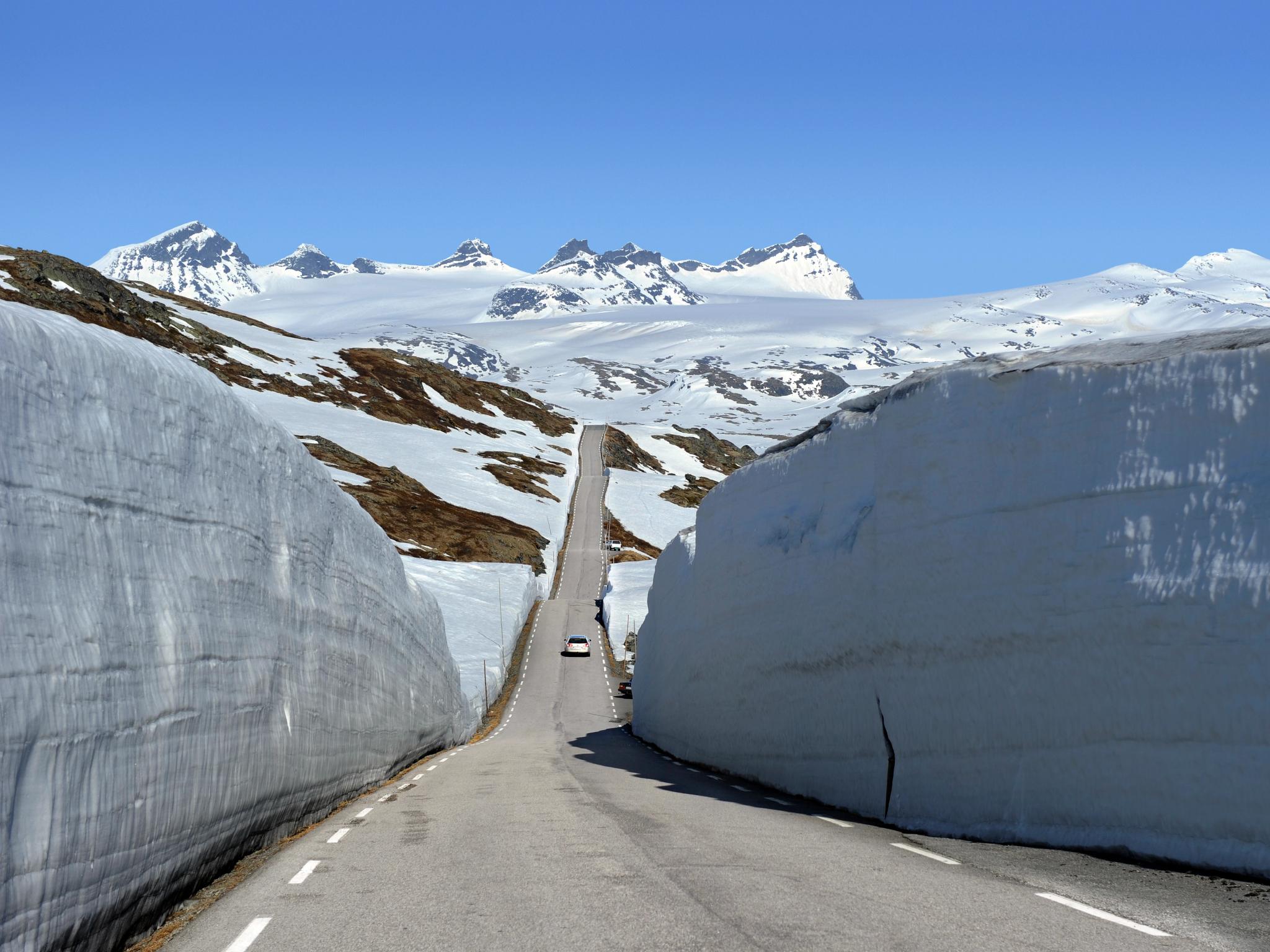 A car between large snow banks on Norwegian Scenic Route Sognefjellet, Fjord Norway