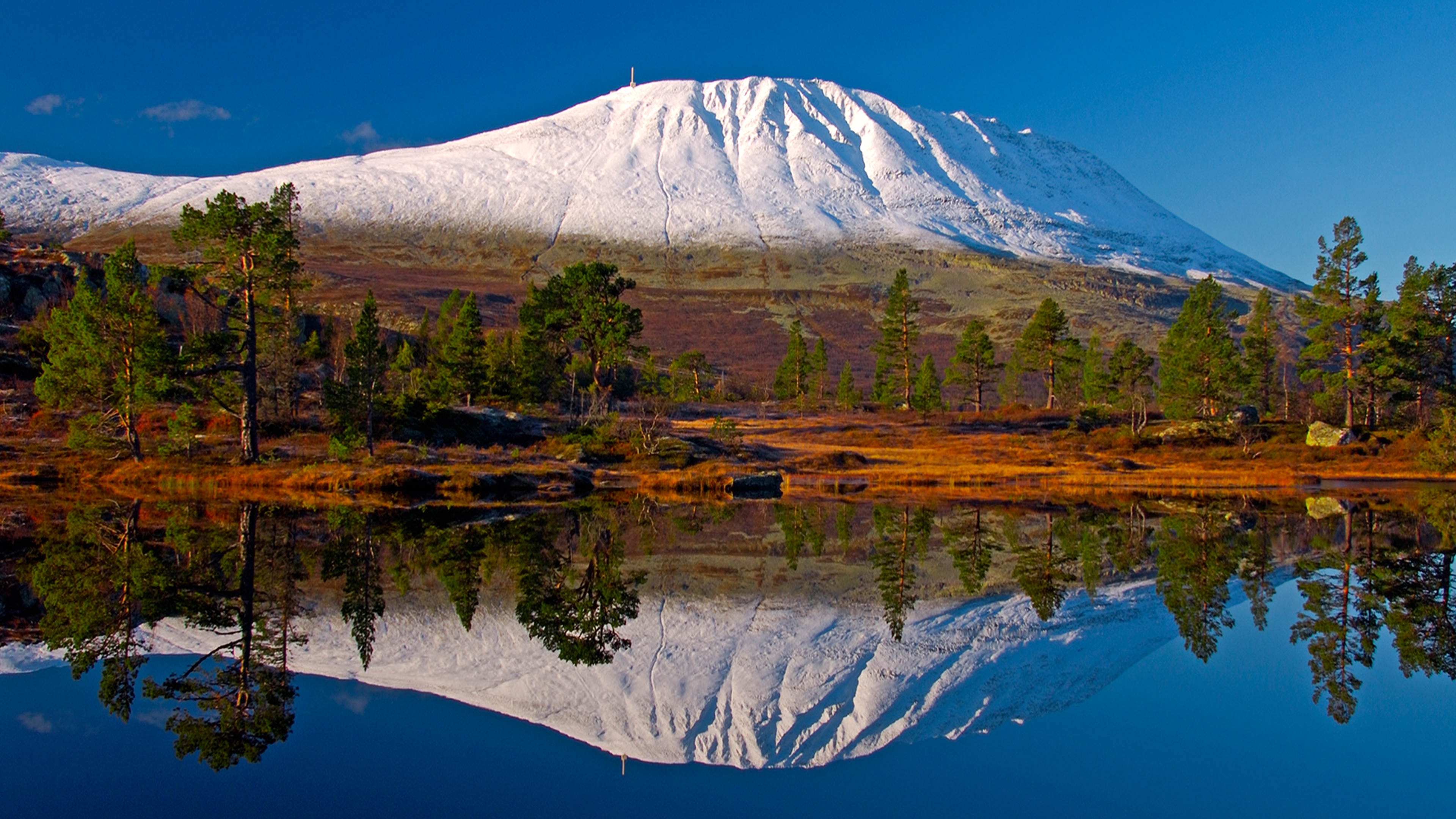 Der schneebedeckte Berg Gaustatoppen spiegelt sich in einem See. Telemark, Norwegen