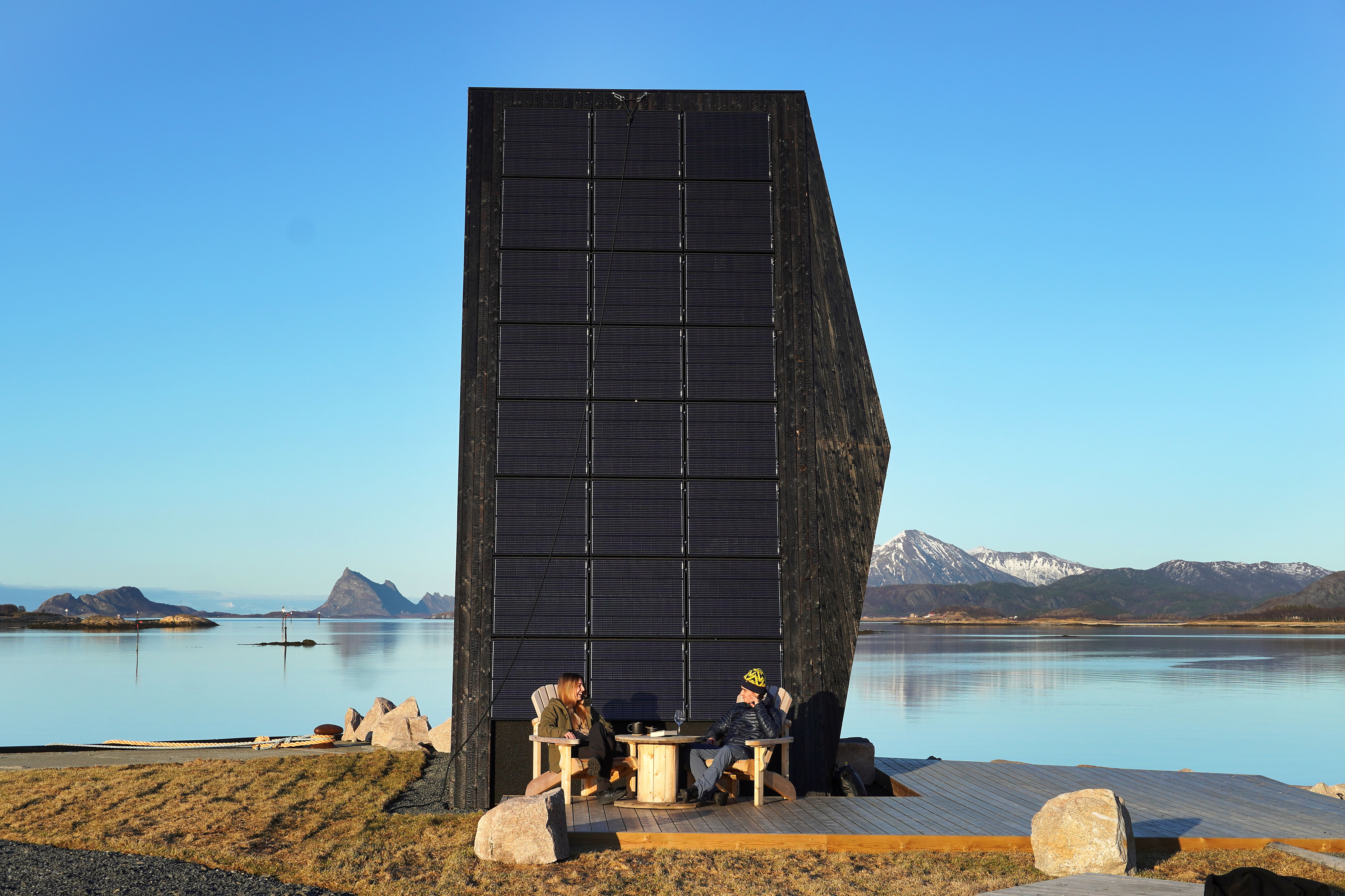 Two people in front of a modern cabin by the sea