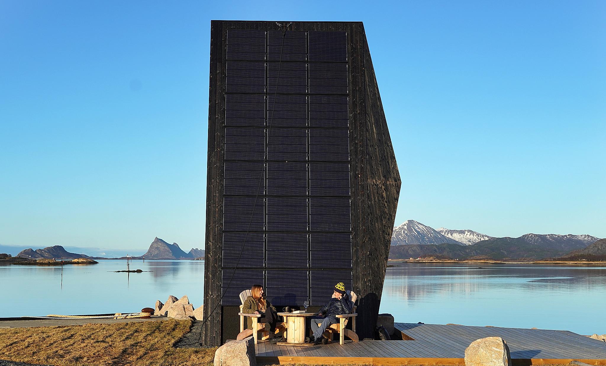 Two people in front of a modern cabin by the sea