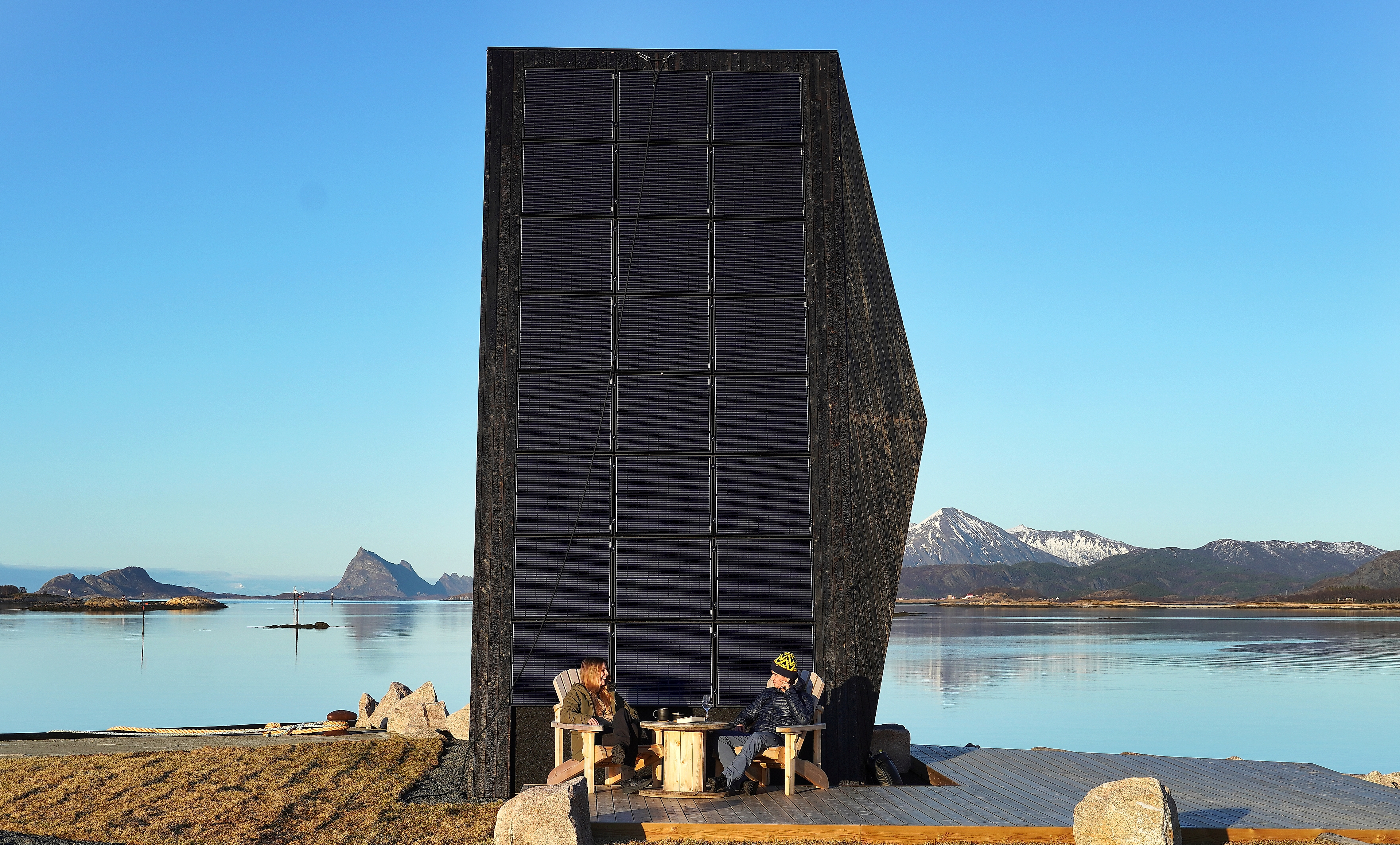 Two people in front of a modern cabin by the sea